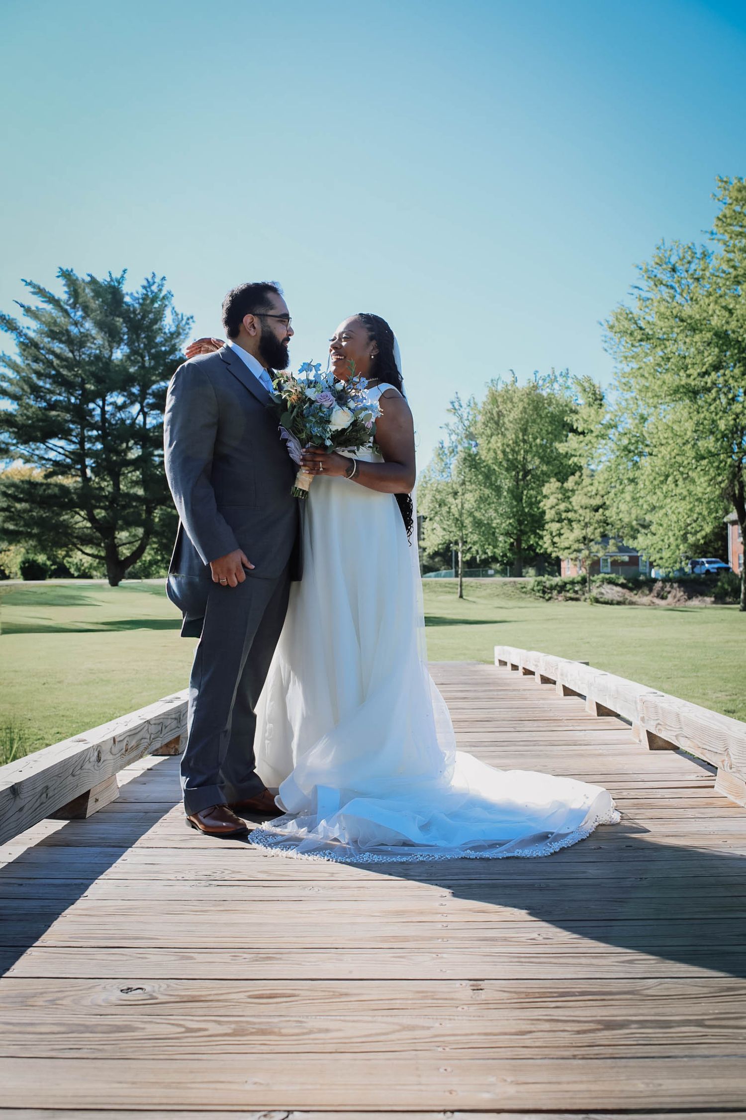 A bride and groom share a romantic moment on a wooden bridge outdoors on their wedding day.