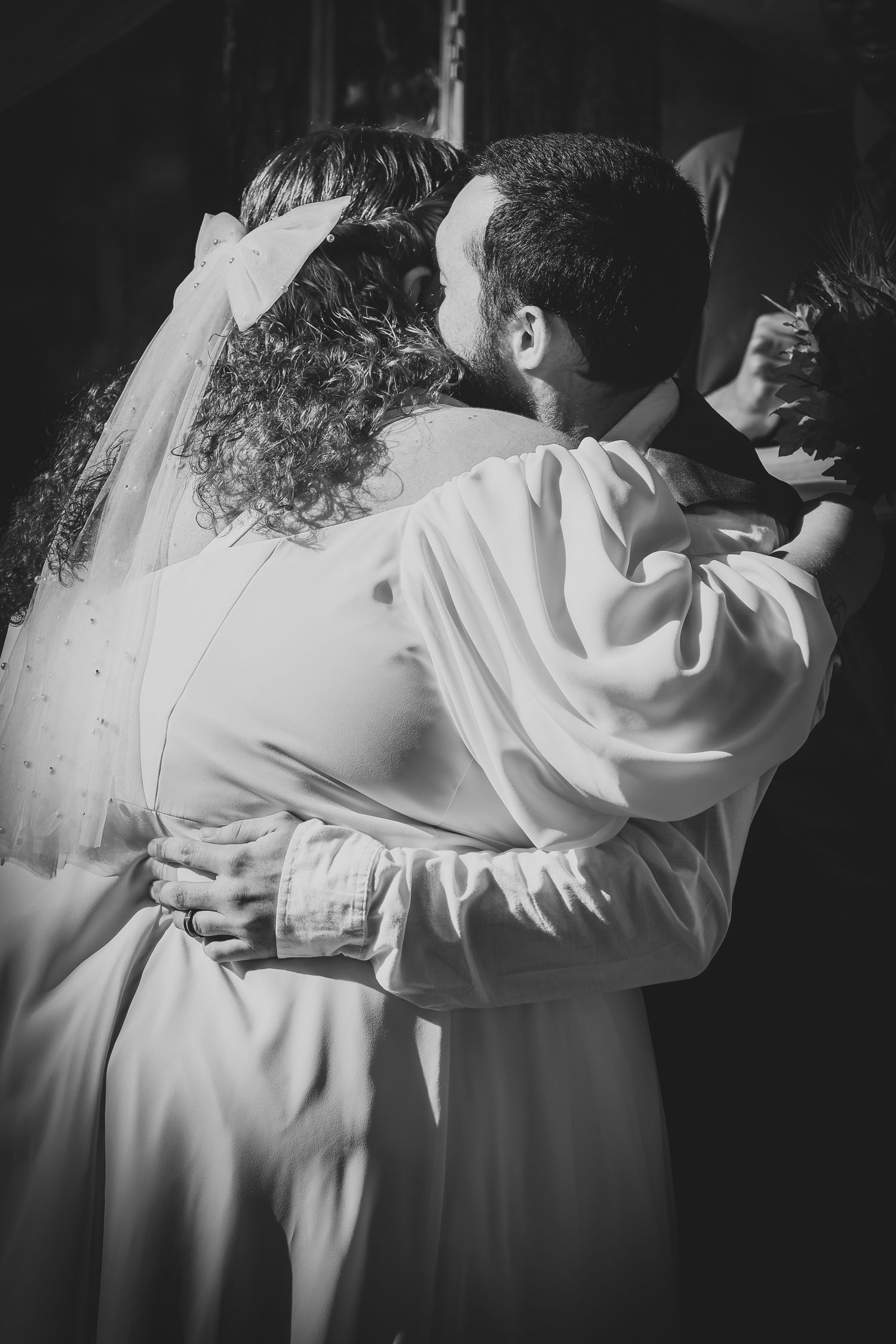 A series of black and white photographs showing people embracing in white robes, creating a tender emotional moment.