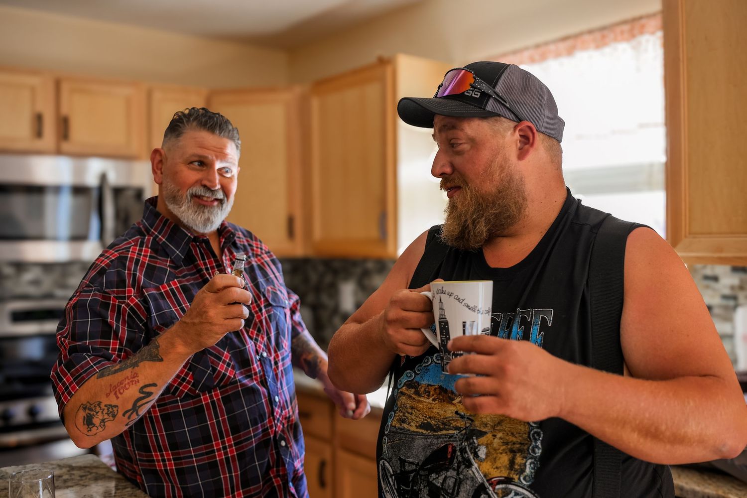 Two people share a moment over coffee in a kitchen with wooden cabinets in the background.
