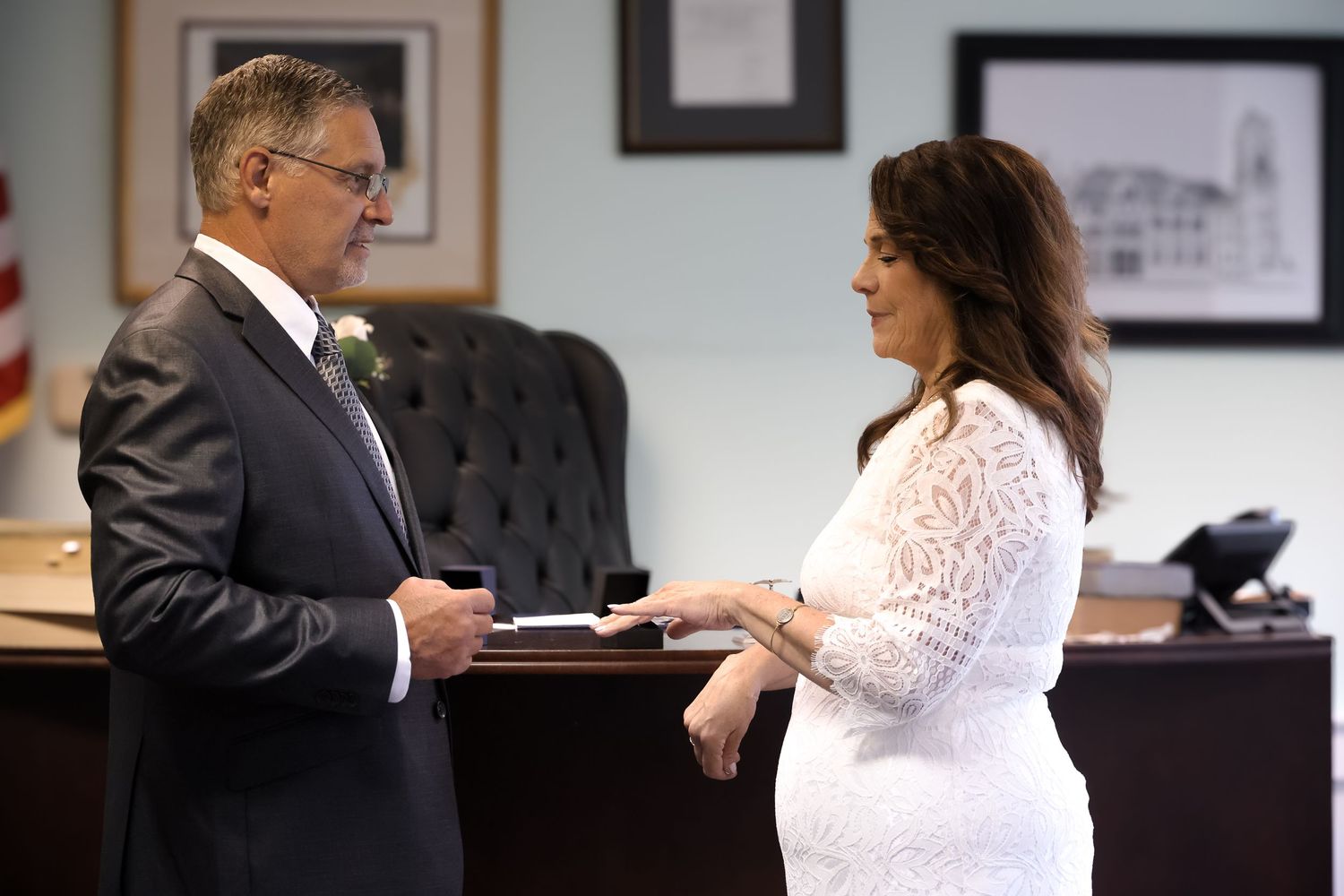 A couple in formal attire exchanges rings during a wedding ceremony at a courthouse.