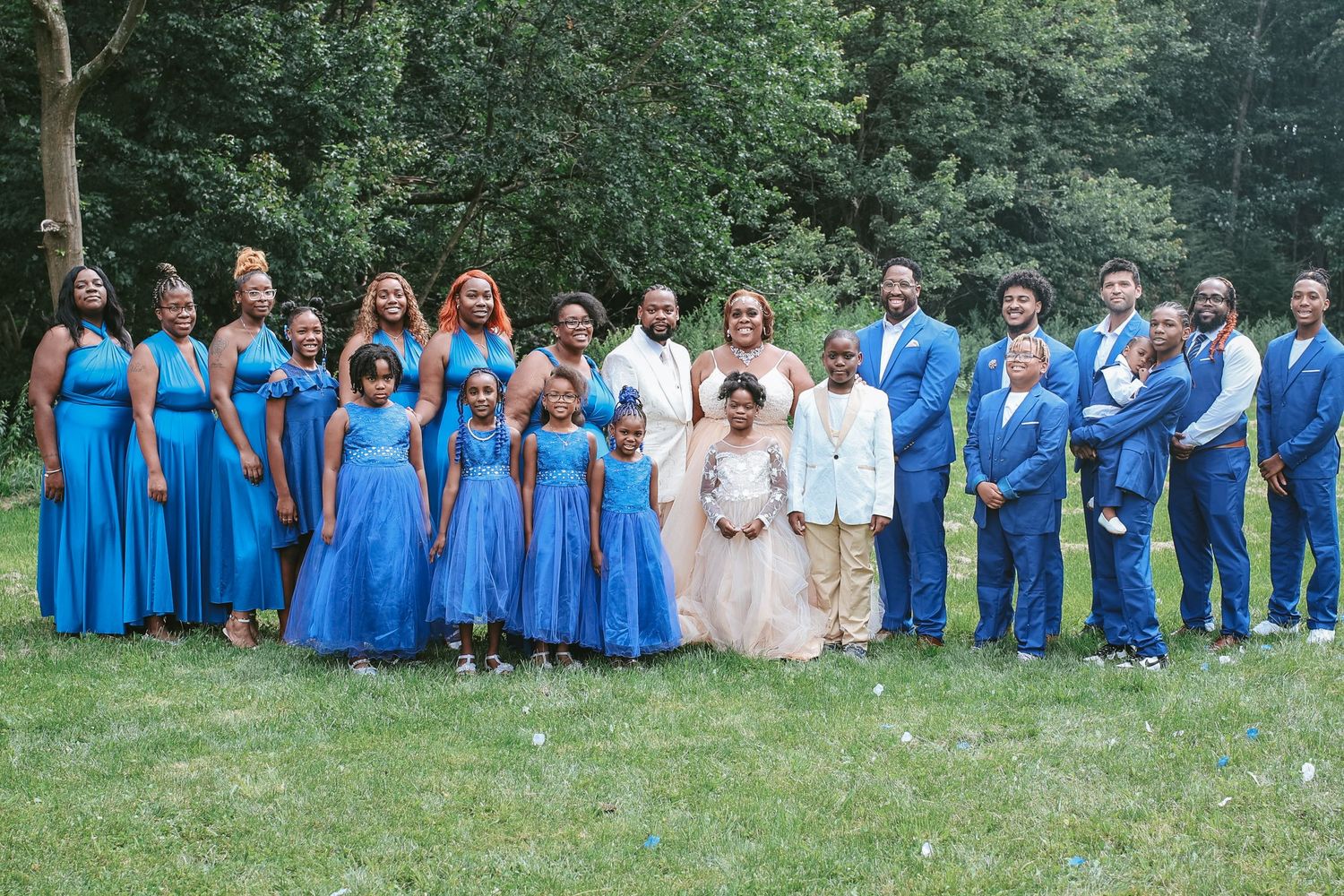 Wedding party wearing bright blue and white dresses poses together outdoors in a garden setting.