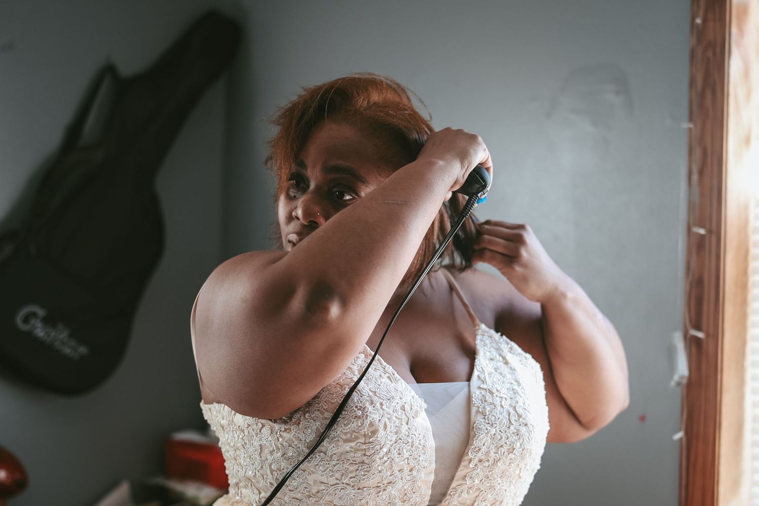 A bride in a white lace wedding dress adjusts her hair while getting ready for her special day.