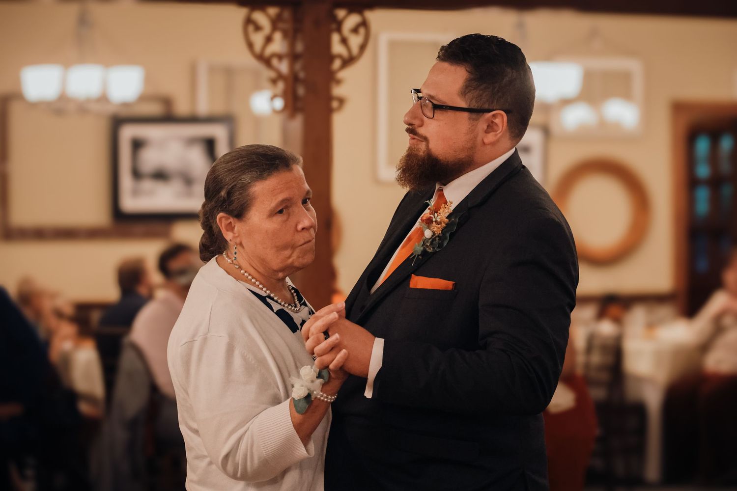 A couple embraces during a romantic dance at an indoor wedding celebration with warm ambient lighting.