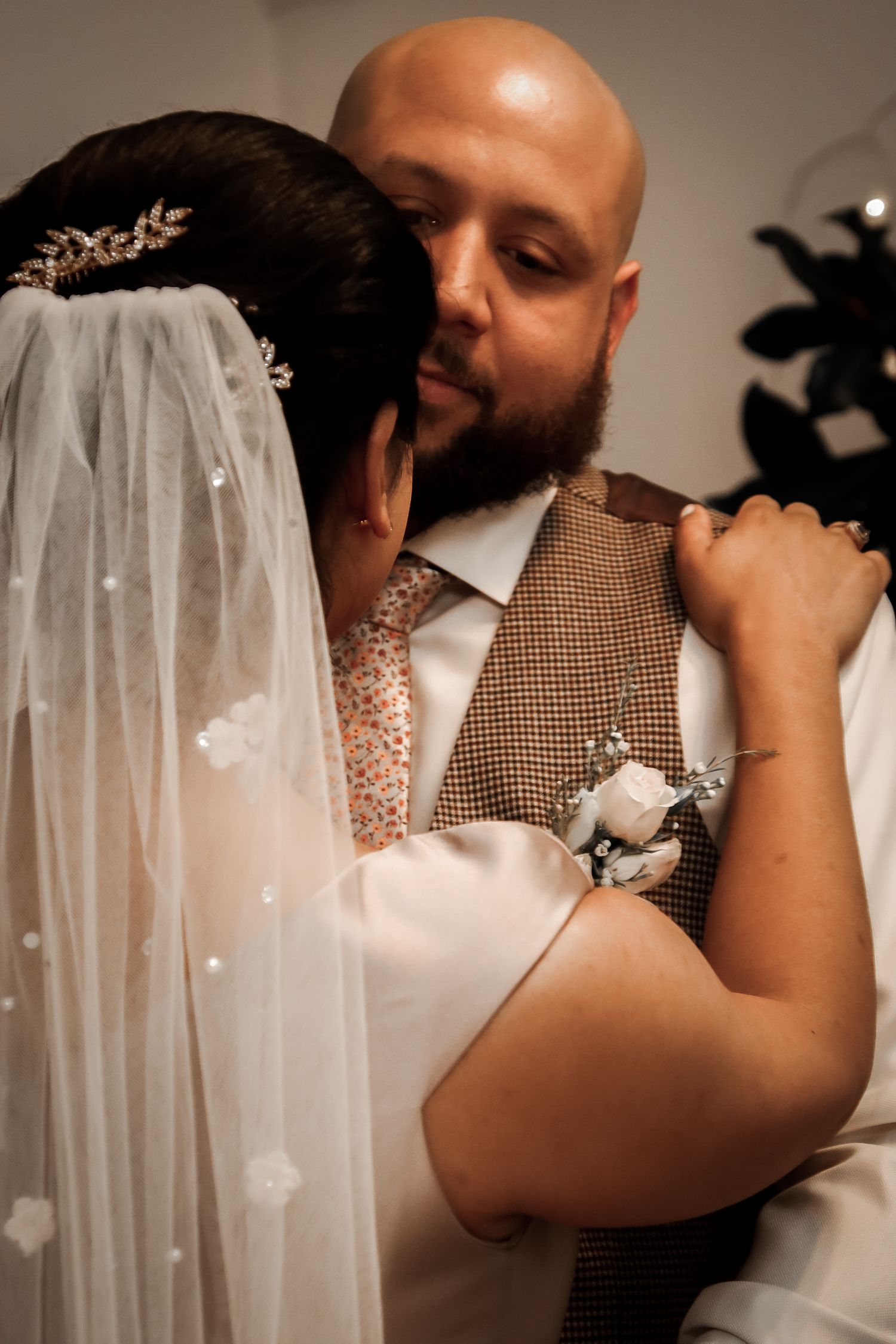 Intimate wedding moment captured with bride in white veil and groom wearing brown tweed vest and white boutonniere.