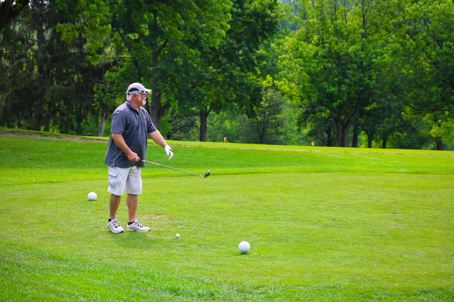 Golfers practice putting on a lush green course surrounded by trees and natural scenery.