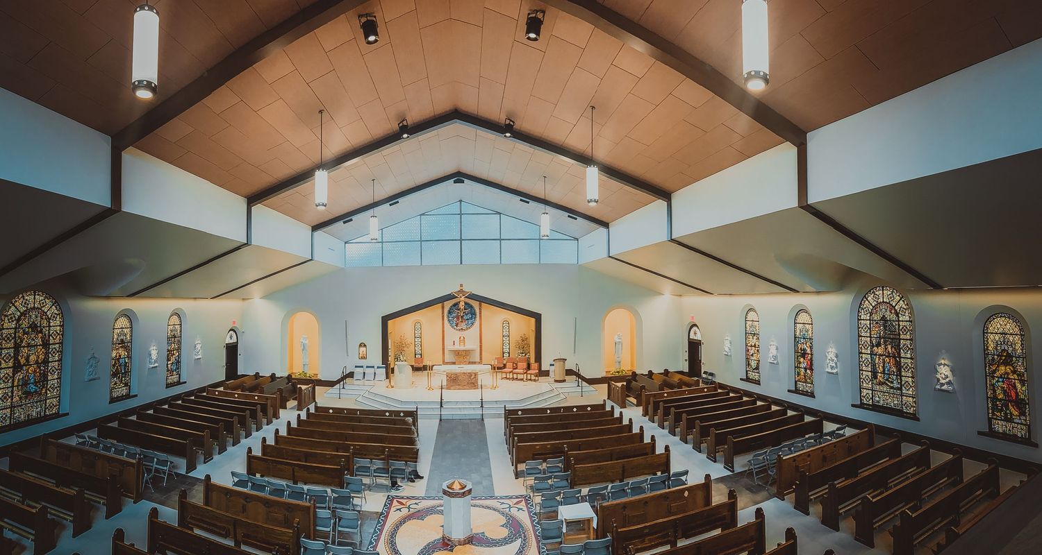 A modern church sanctuary with wooden pews, stained glass windows and vaulted ceilings shown in a panoramic view.