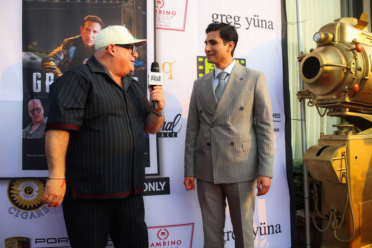 Two people having a conversation at a film event with a vintage diving suit displayed in the background.