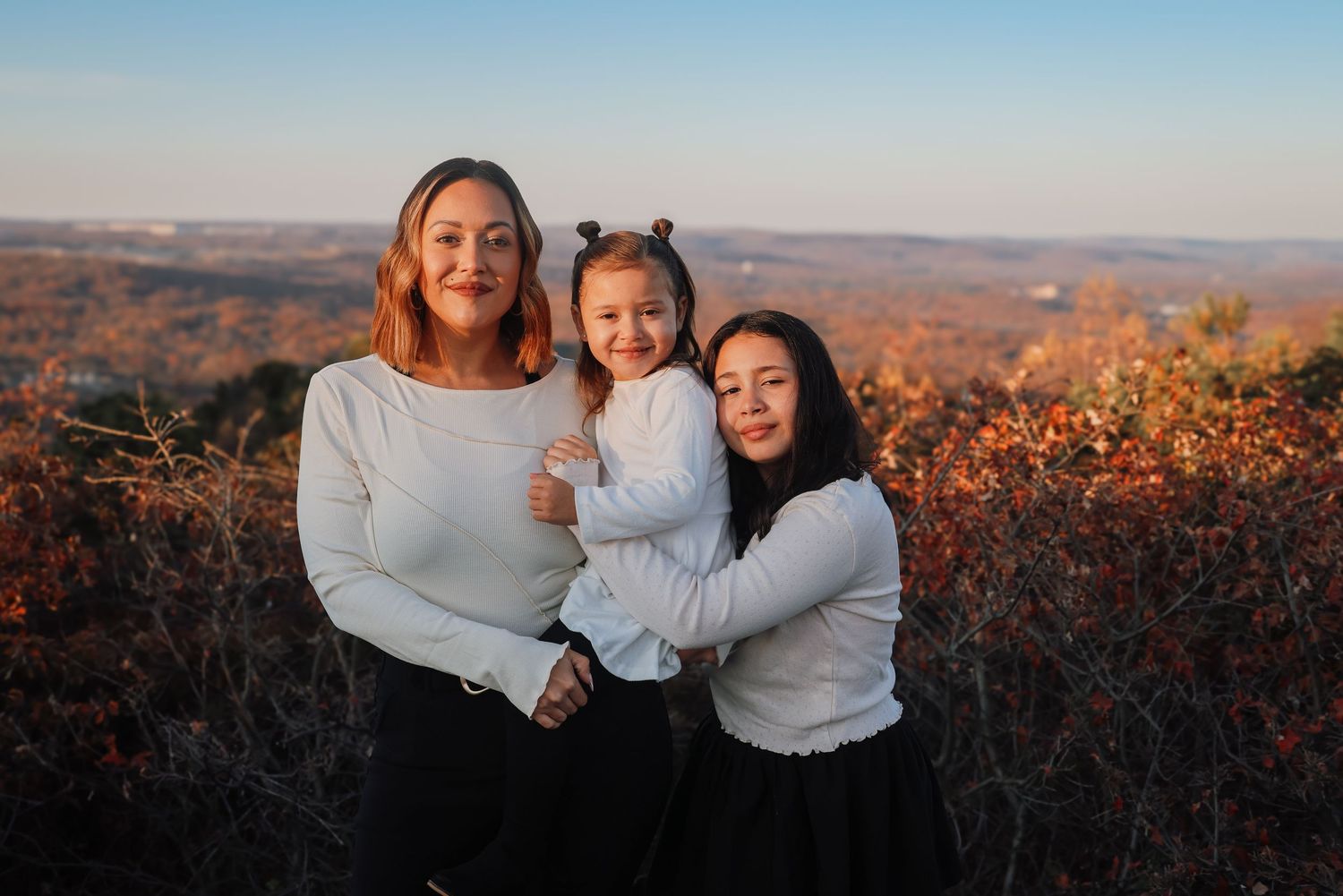 People embracing and smiling together against a scenic autumn mountain backdrop during golden hour.