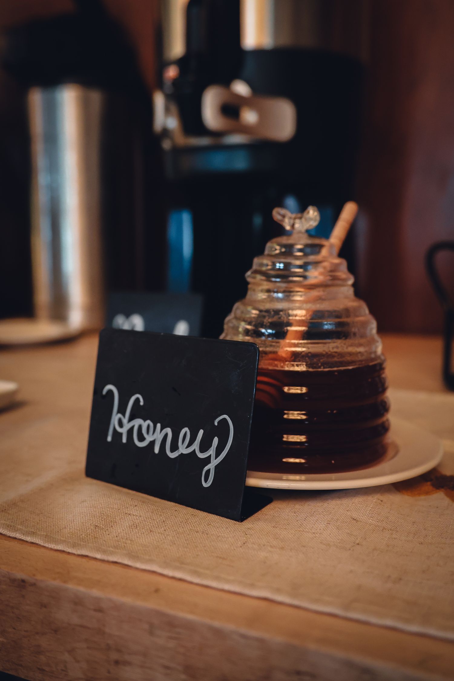 A series of four close-up shots showing a jar of honey with a black label on a rustic wooden table.
