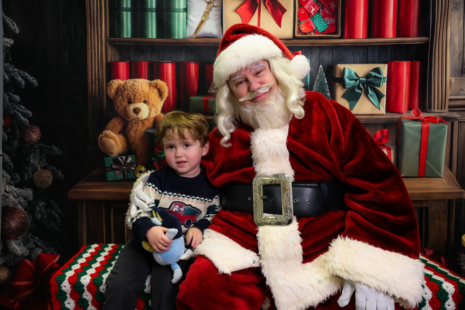 A festive holiday scene shows a person in a traditional red suit and white beard seated with a small child.