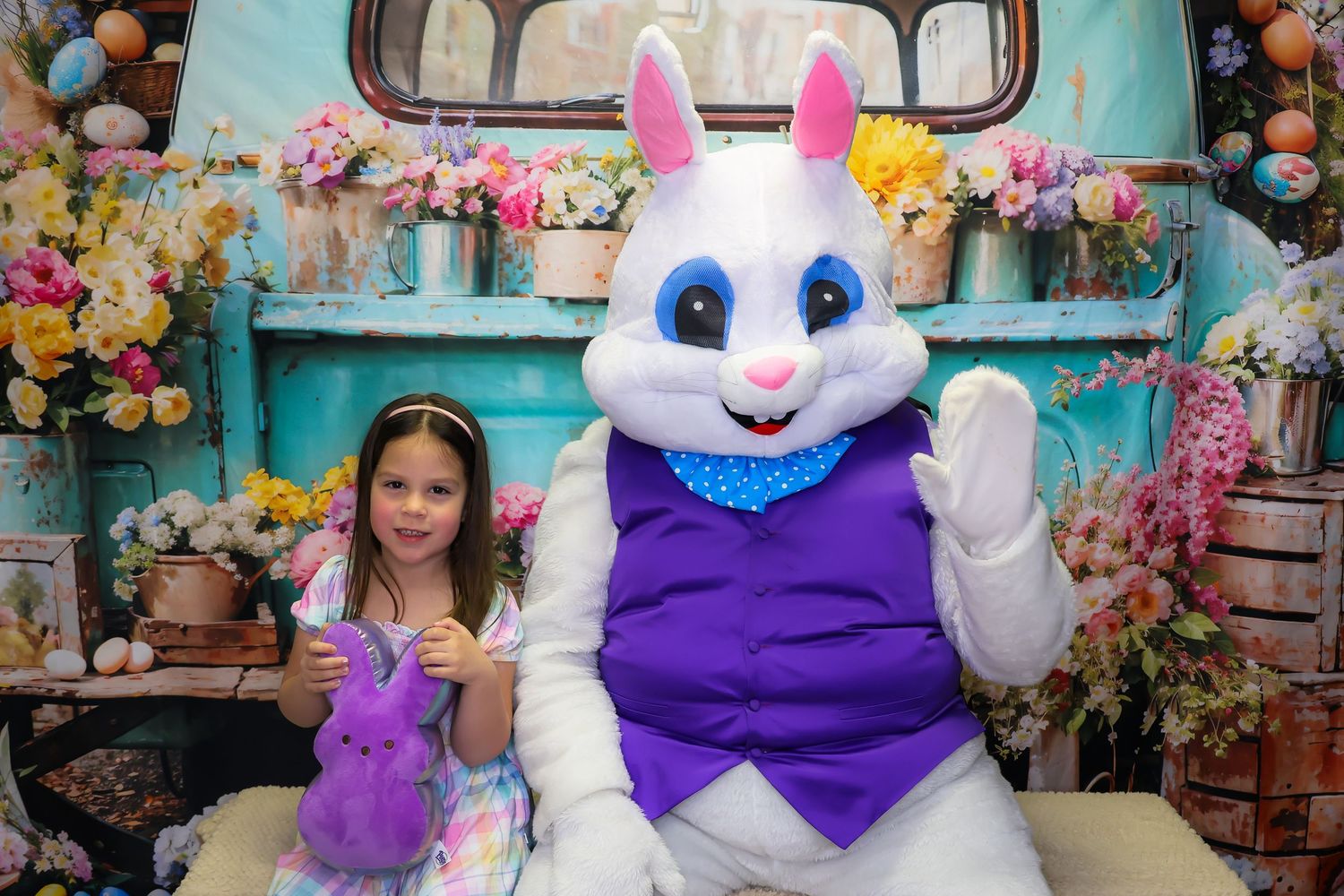 Easter Bunny mascot in purple vest poses with colorful spring decorations and plush toys in retail setting.
