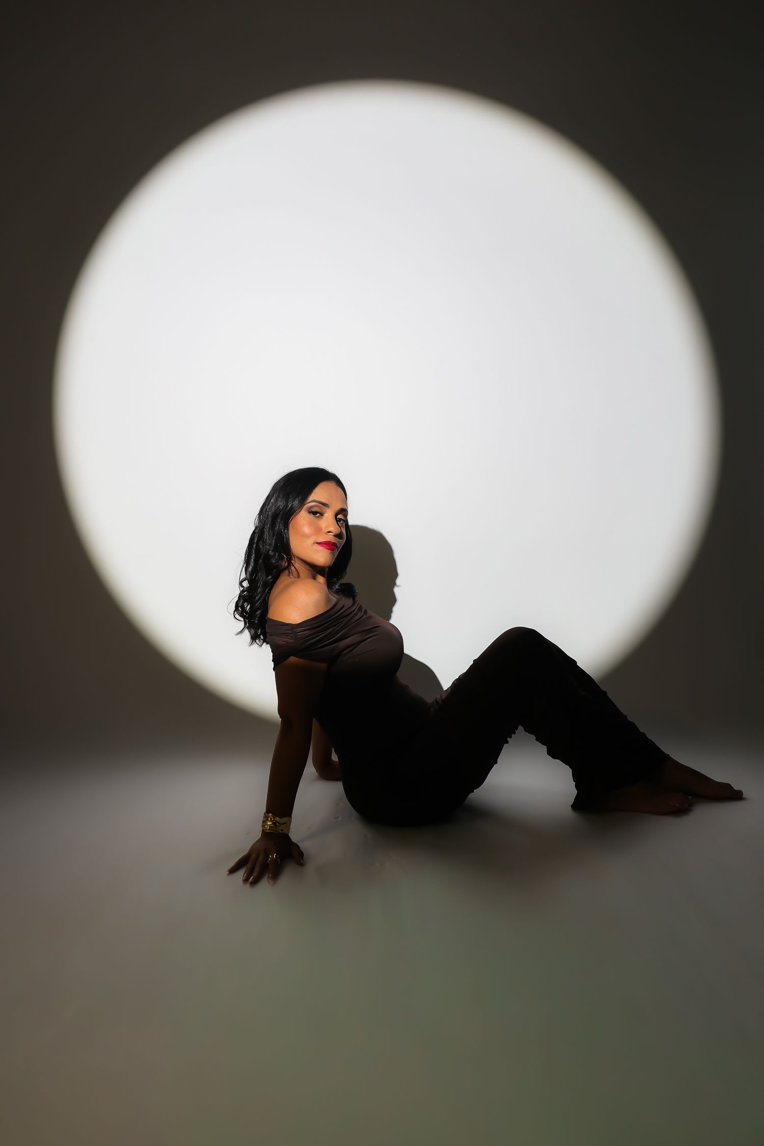 A person poses against a dark background with dramatic circular spotlight creating artistic silhouette effect.