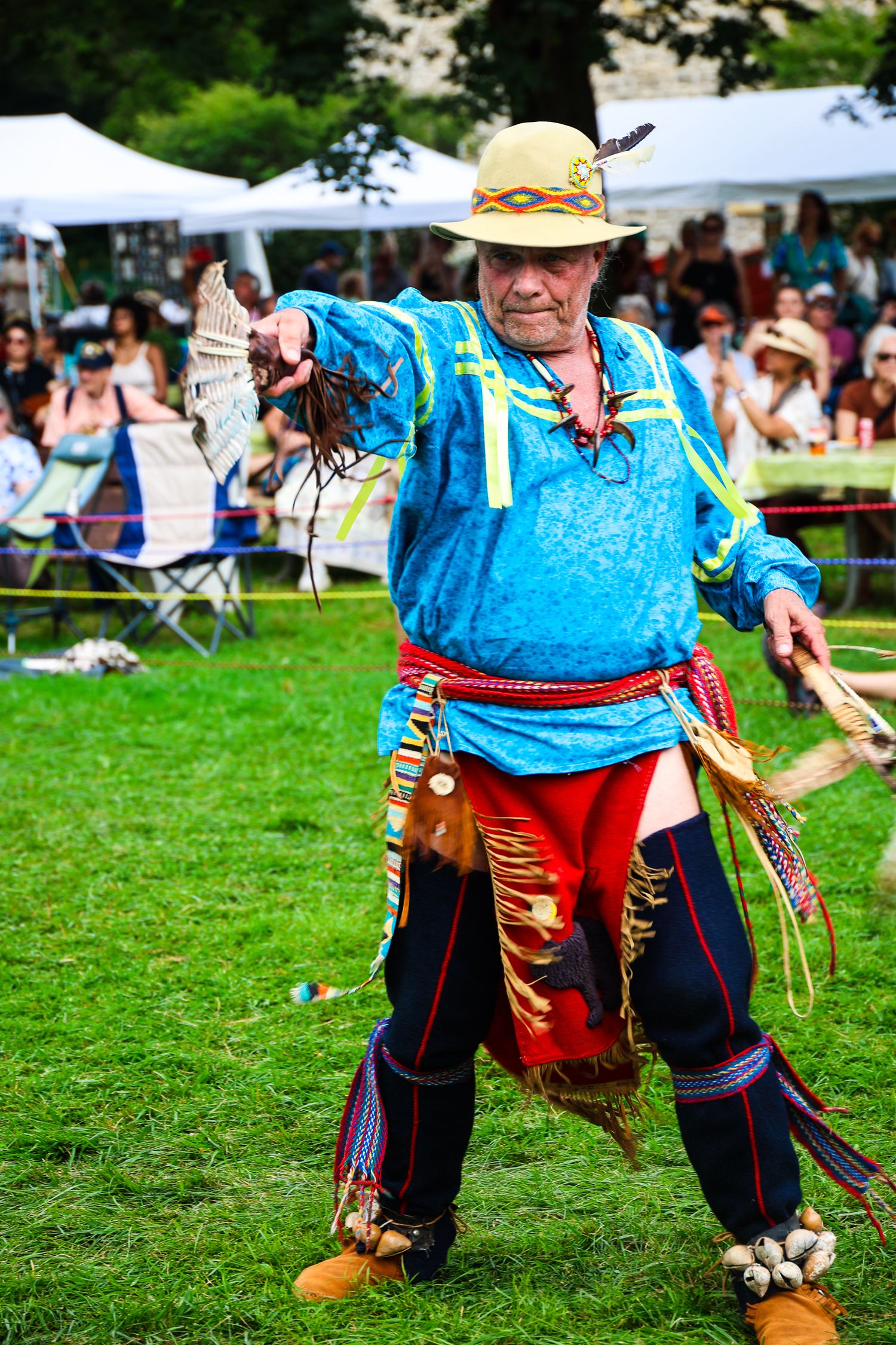 Traditional Morris dancer performs with bells and ribbons on costume at outdoor festival on green grass.