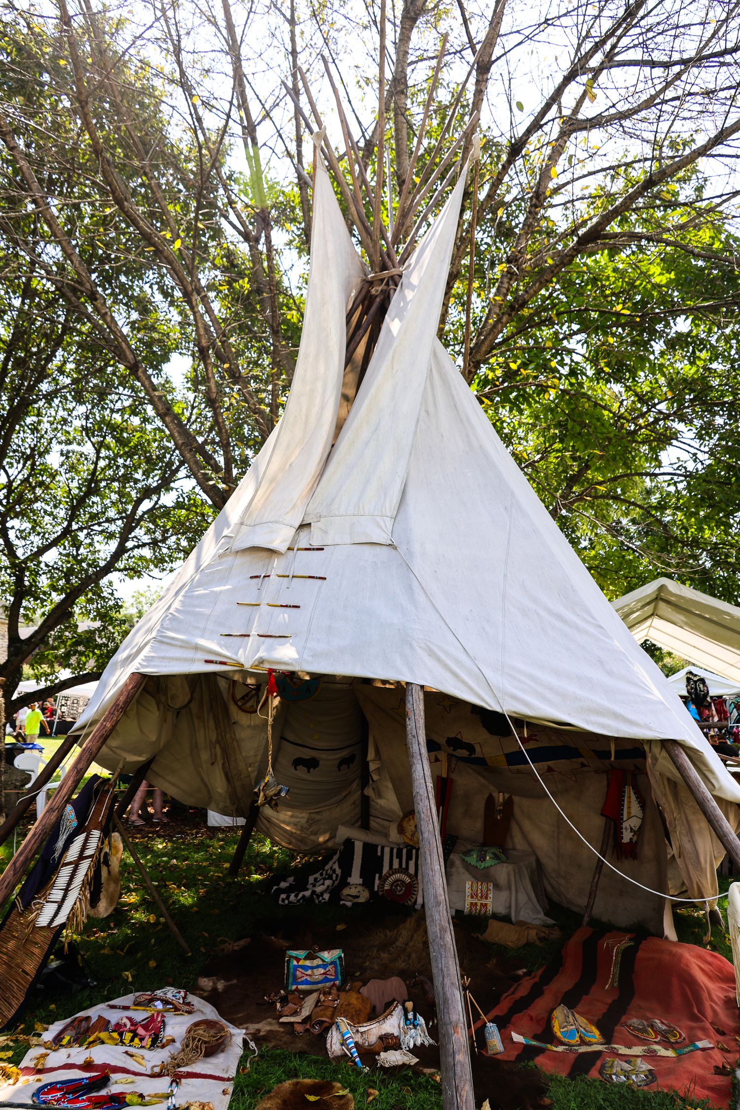 A traditional white teepee tent set up outdoors with blankets and supplies visible inside through the entrance.