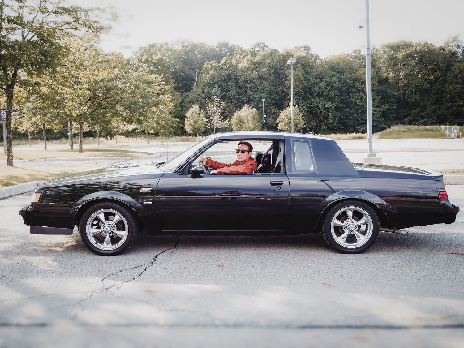 A black Buick Grand National muscle car parked on a tree-lined street during daytime.