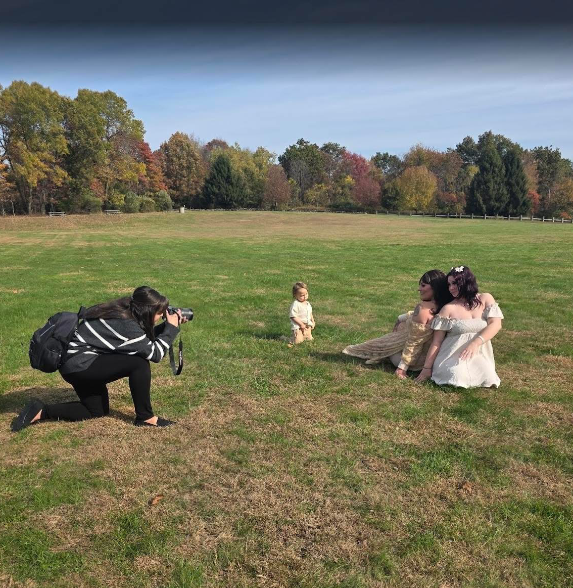 Photographers at work in an open field with fall foliage in background.