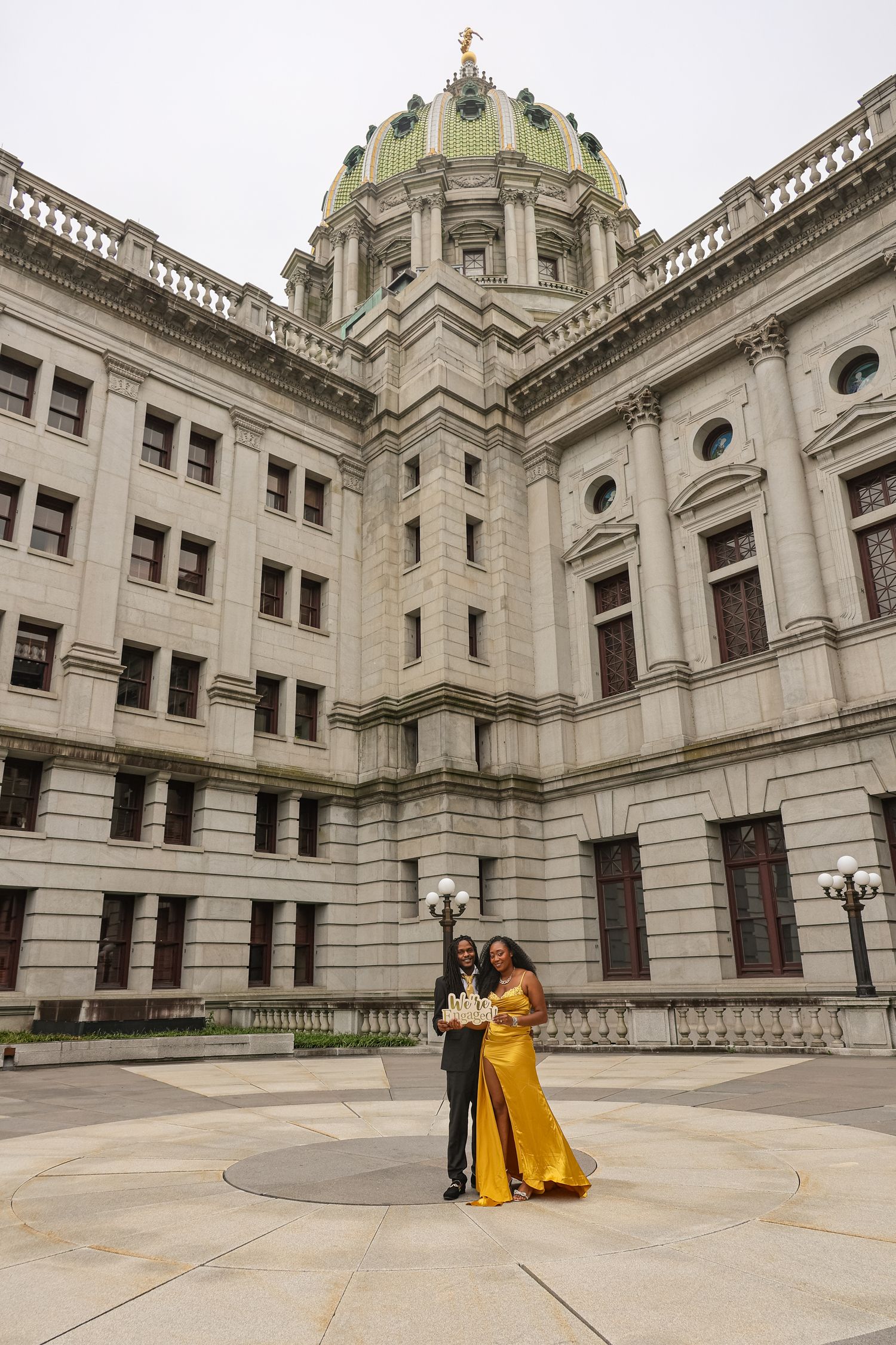 Couple posing for photos in front of the grand Pennsylvania State Capitol building in Harrisburg on a sunny day.