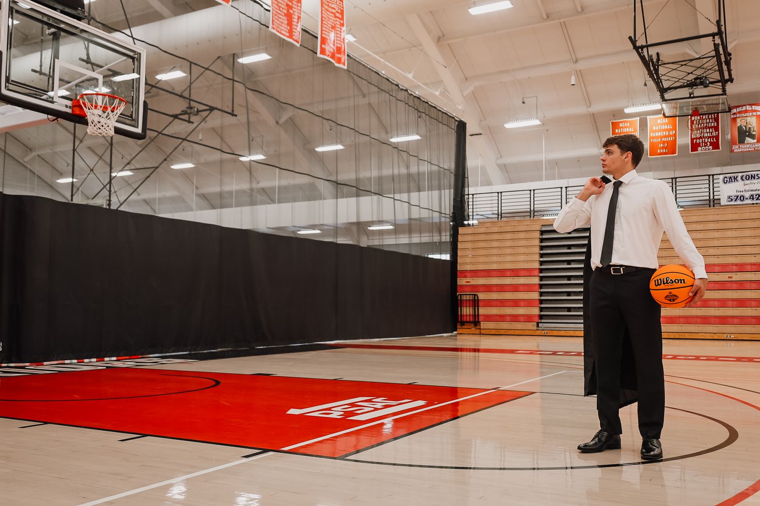 Man in formal attire holding a basketball on a red and white indoor basketball court.