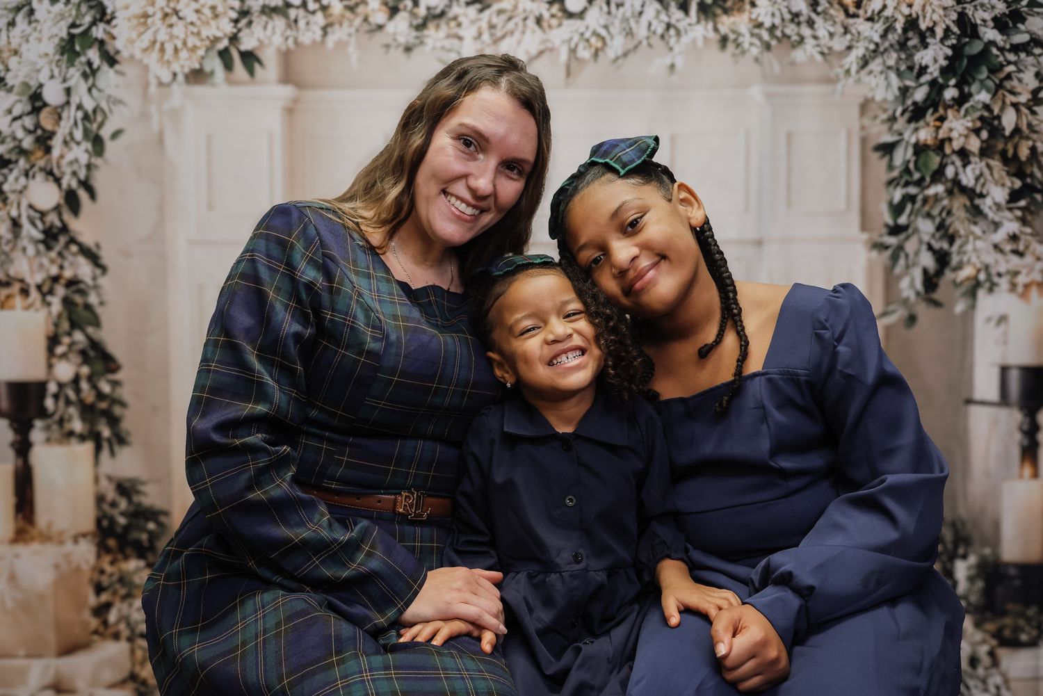 A woman and two children smile together in a festive holiday portrait with white floral decor.