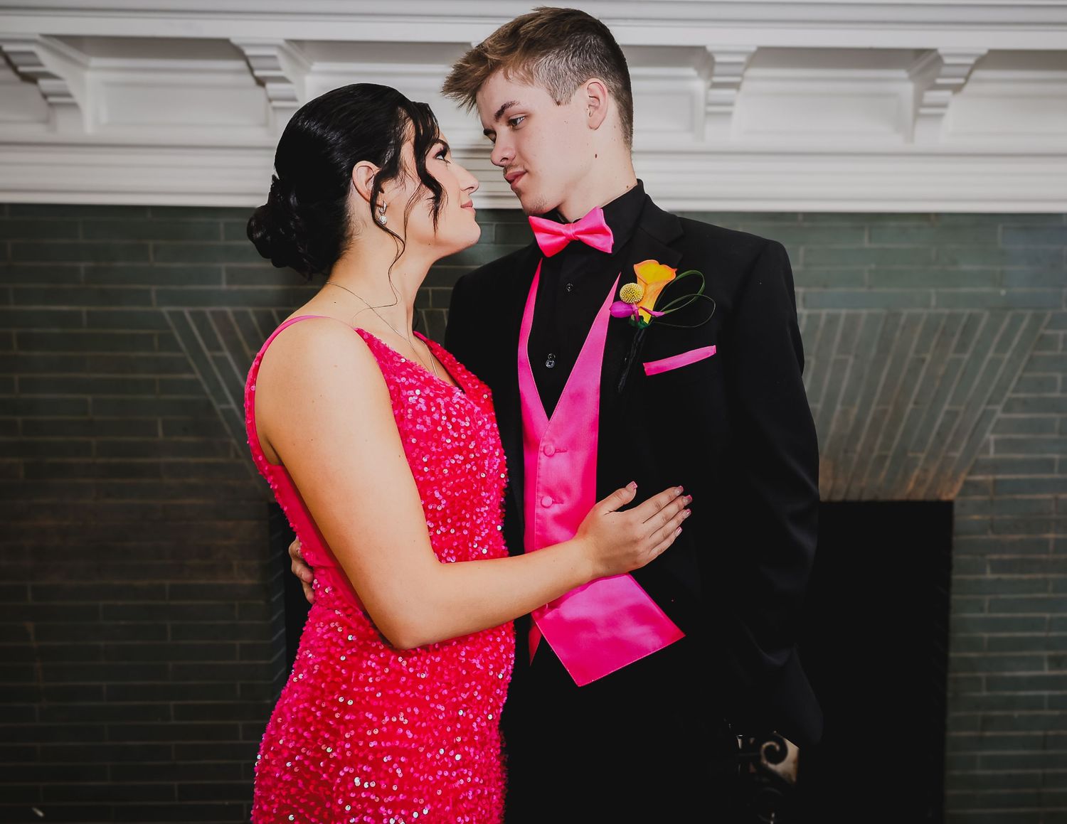 Couple in matching hot pink and black prom attire sharing a romantic moment at a formal dance event.