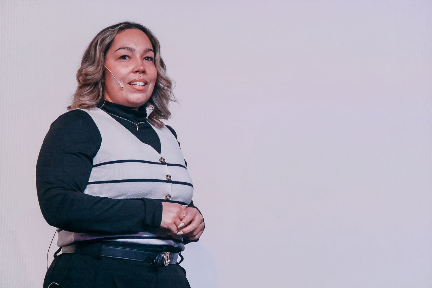 Smiling plus-size woman in black turtleneck and striped vest posing against a light gray background.