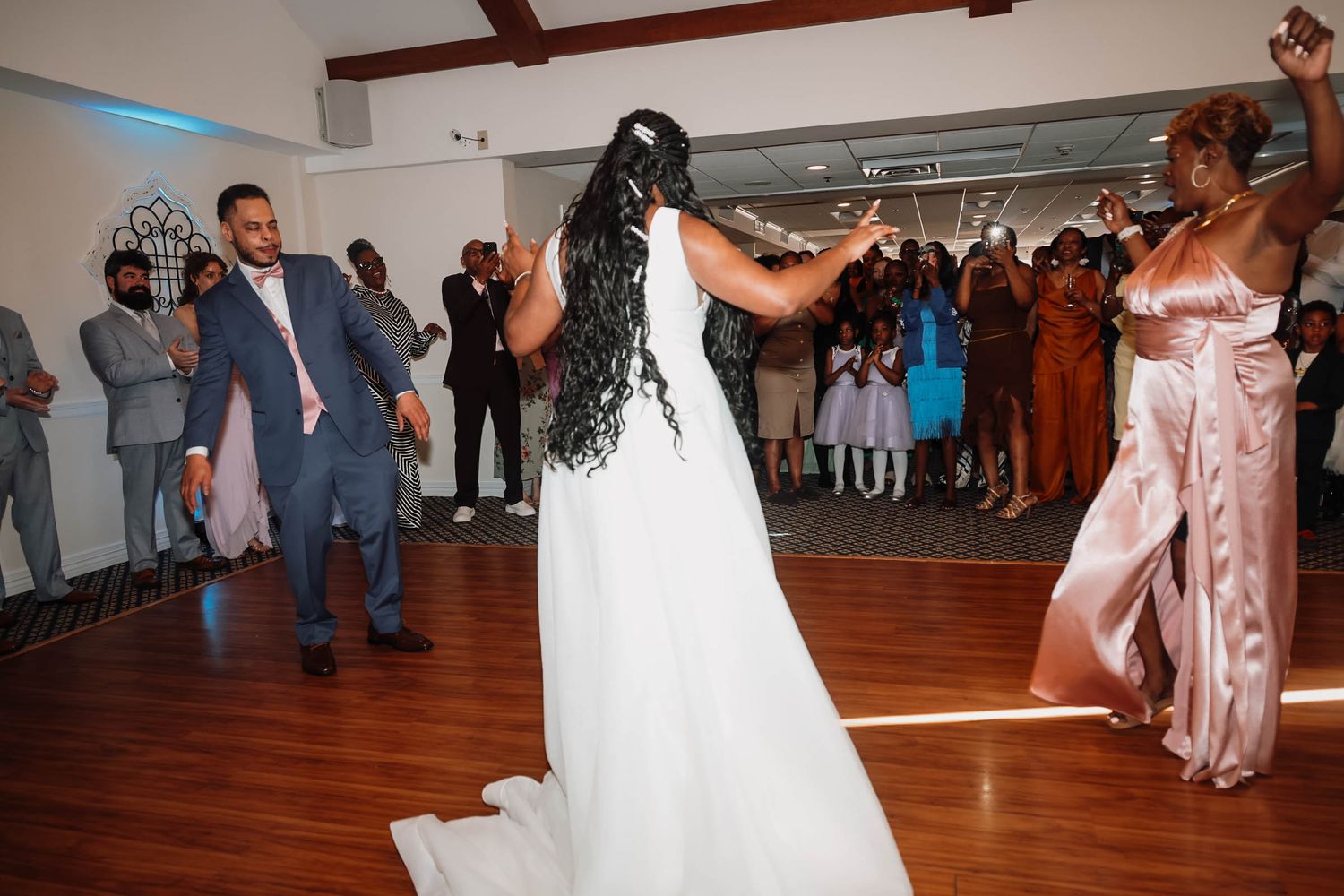 Bride in white gown dances joyfully with guests in elegant wedding reception venue.