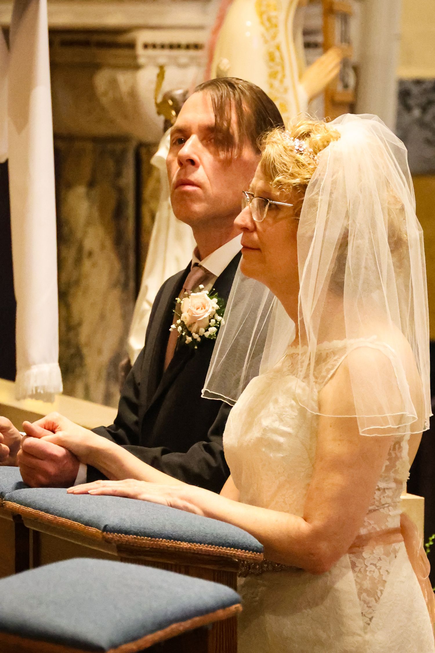 A bride and groom sit together during their wedding ceremony in a traditional church setting.
