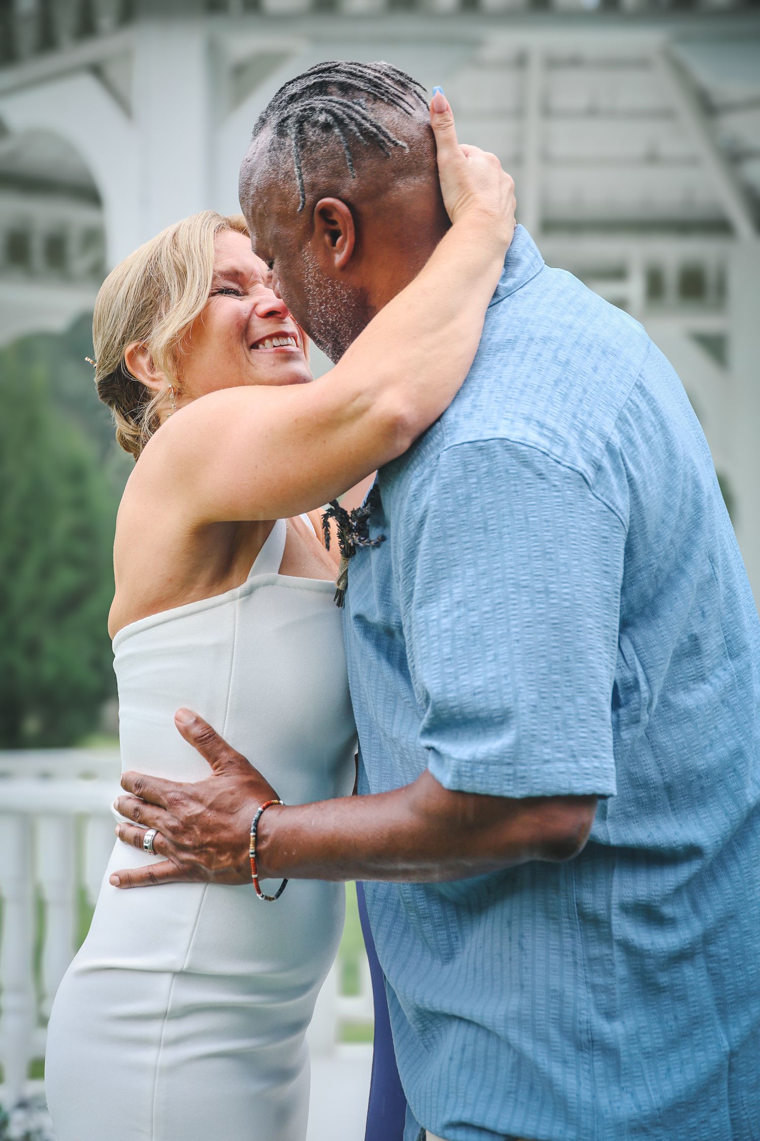 A couple in a blue shirt and white dress embrace and kiss outdoors in a romantic sequence of photos.