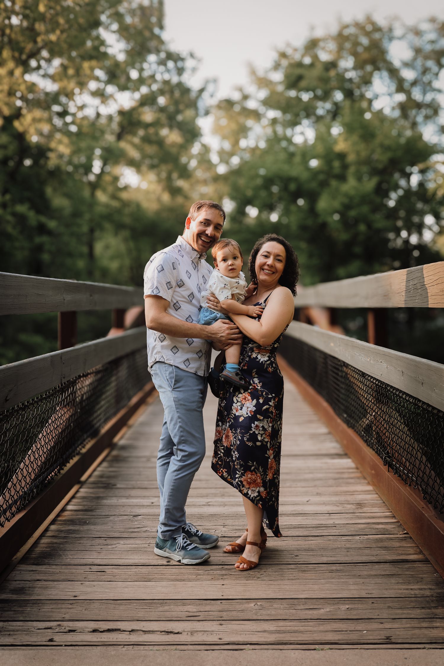A couple shares a romantic moment on a wooden bridge surrounded by trees during a sunset photo session.