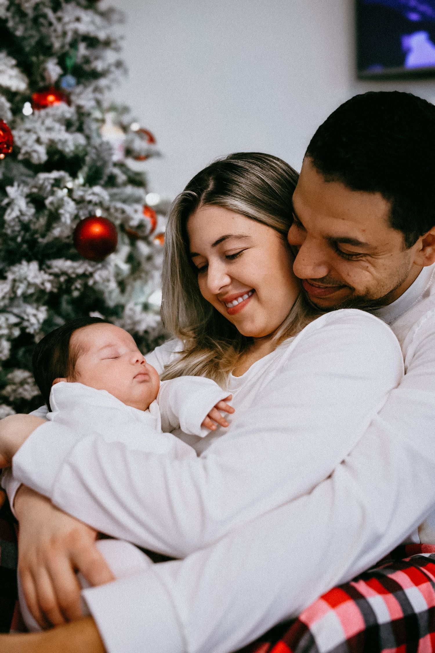 A family shares tender moments in matching white outfits while posing near a decorated Christmas tree.