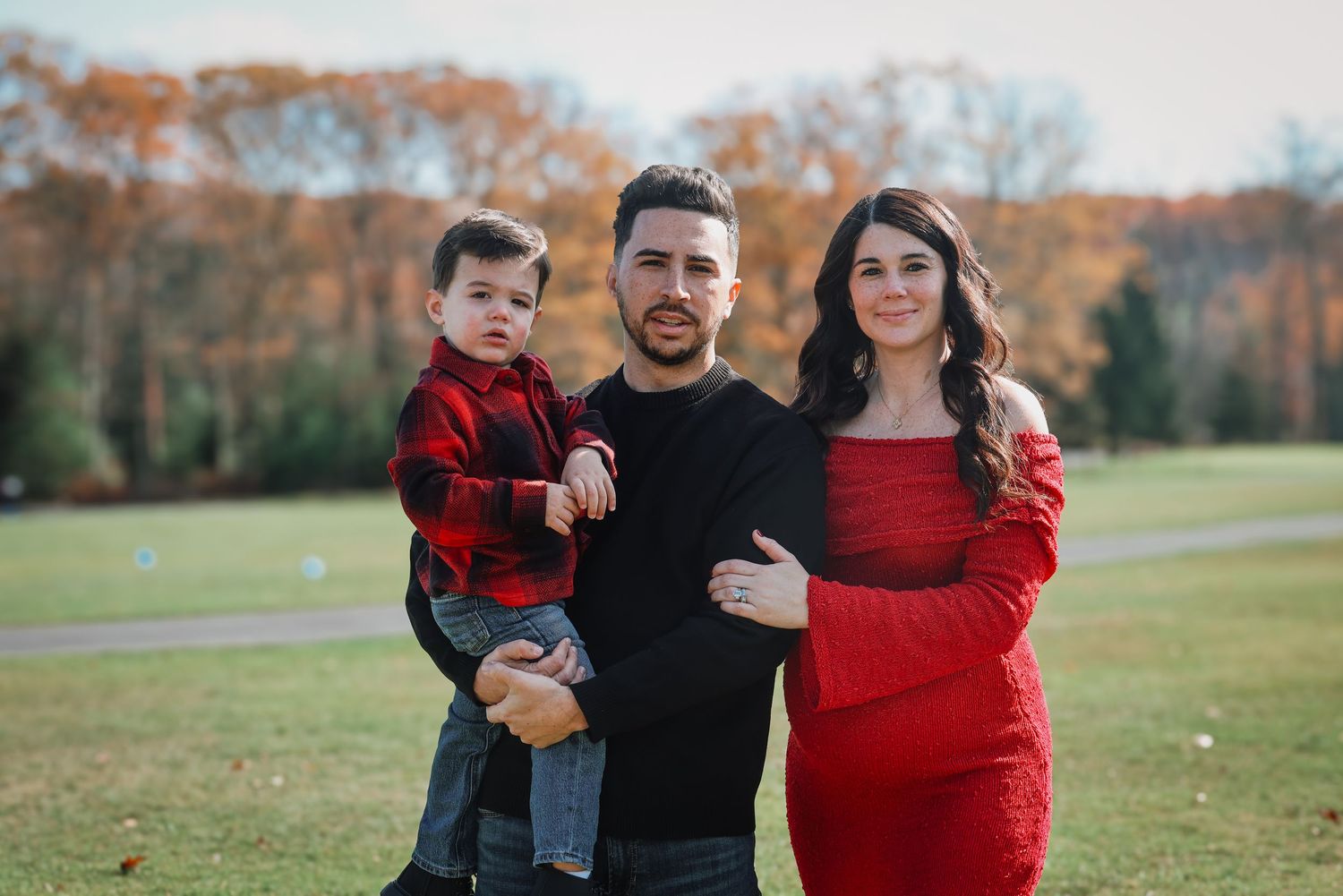 A family wearing coordinating red and black outfits poses together in an autumn field during a photo session.