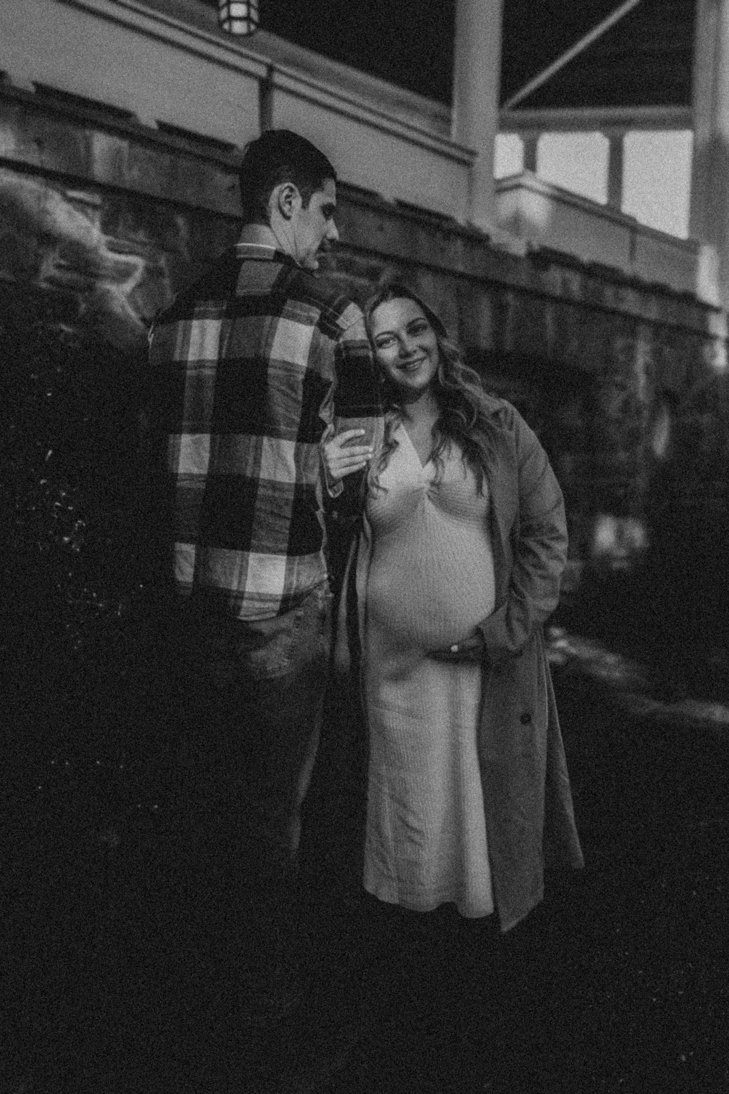 A couple in casual attire poses together outdoors in black and white photography.