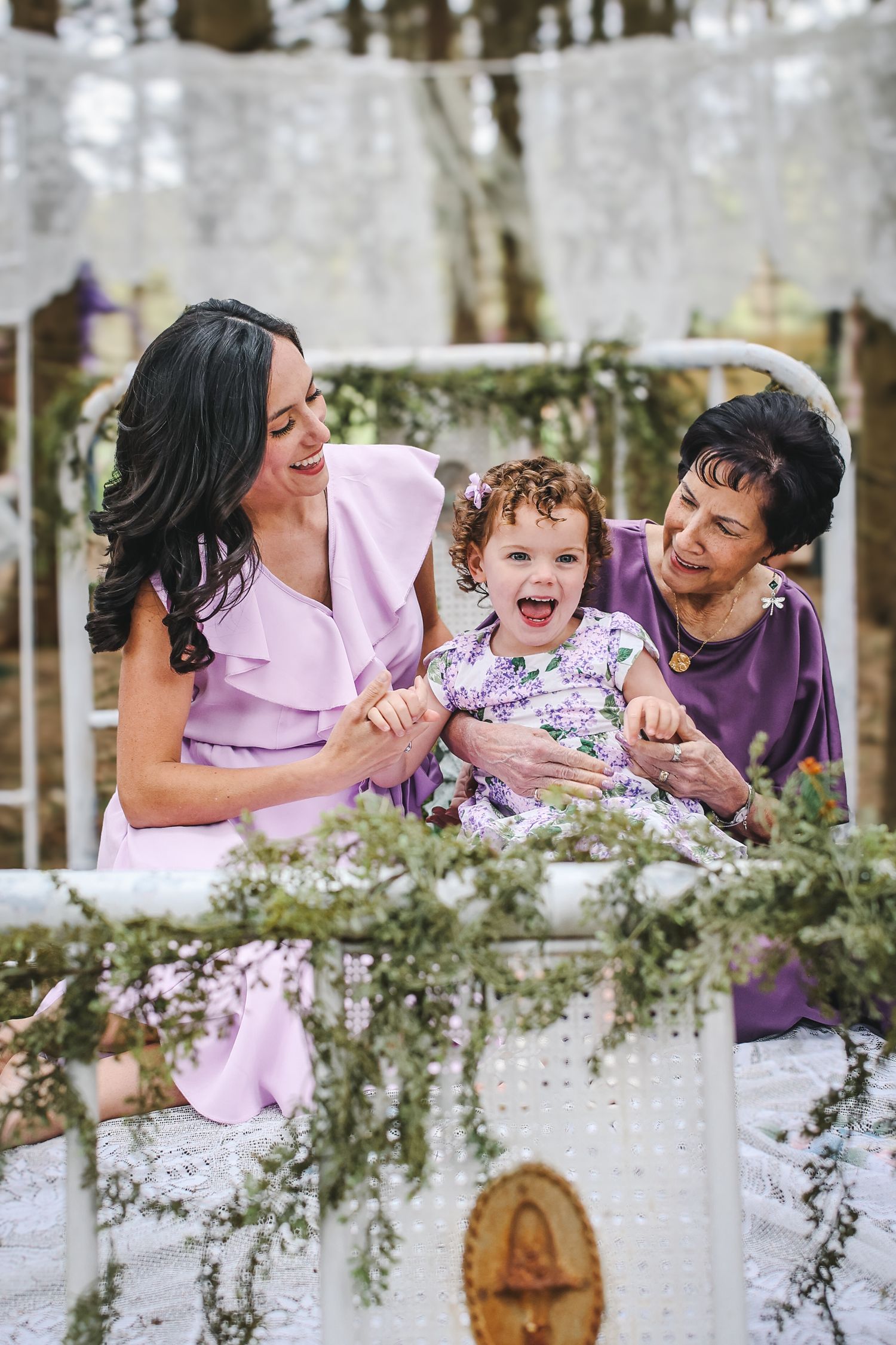 Three generations share a joyful moment together amidst white floral decorations in an outdoor garden setting.
