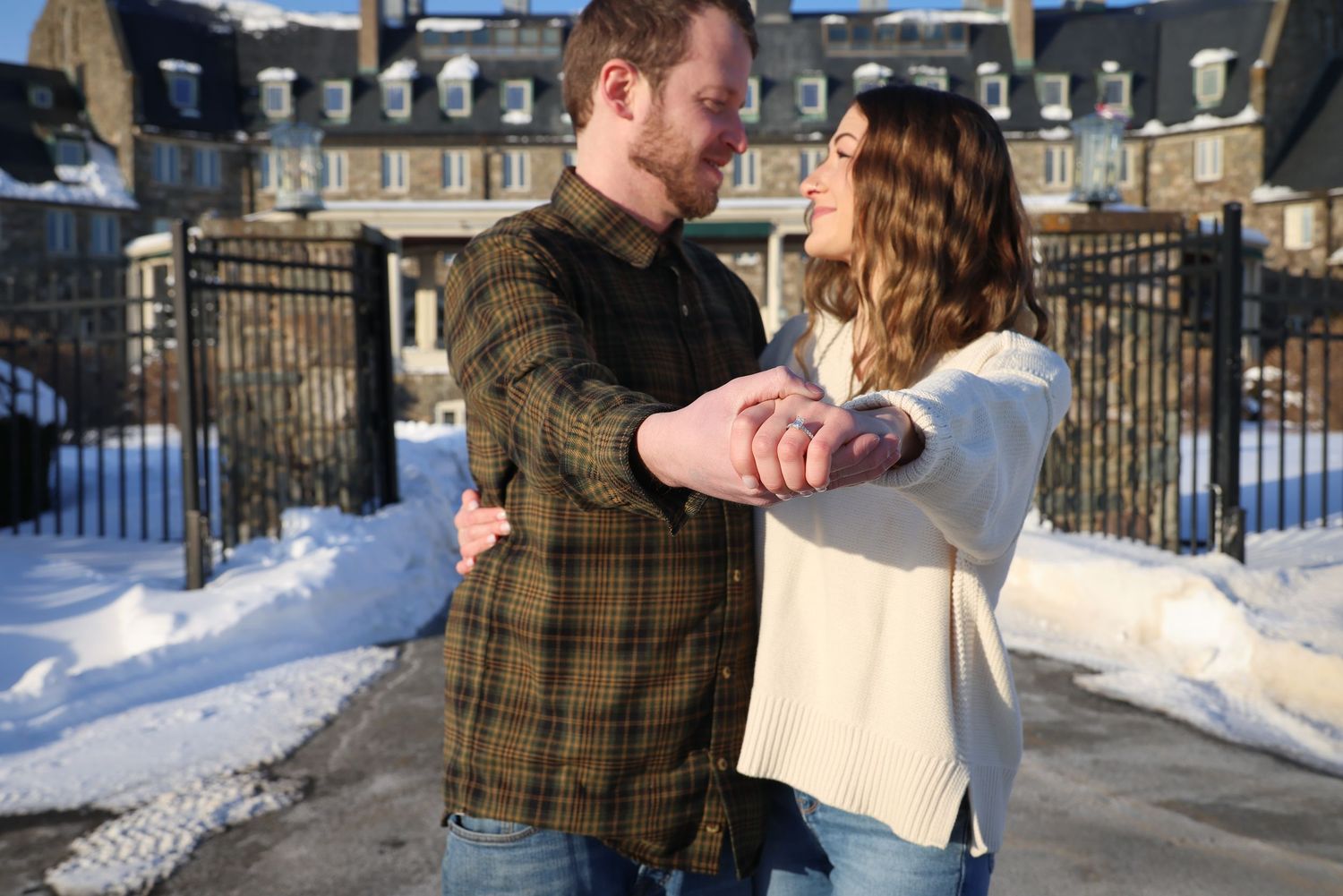 A couple shares a romantic dance together in a snowy winter setting with historic buildings in the background.