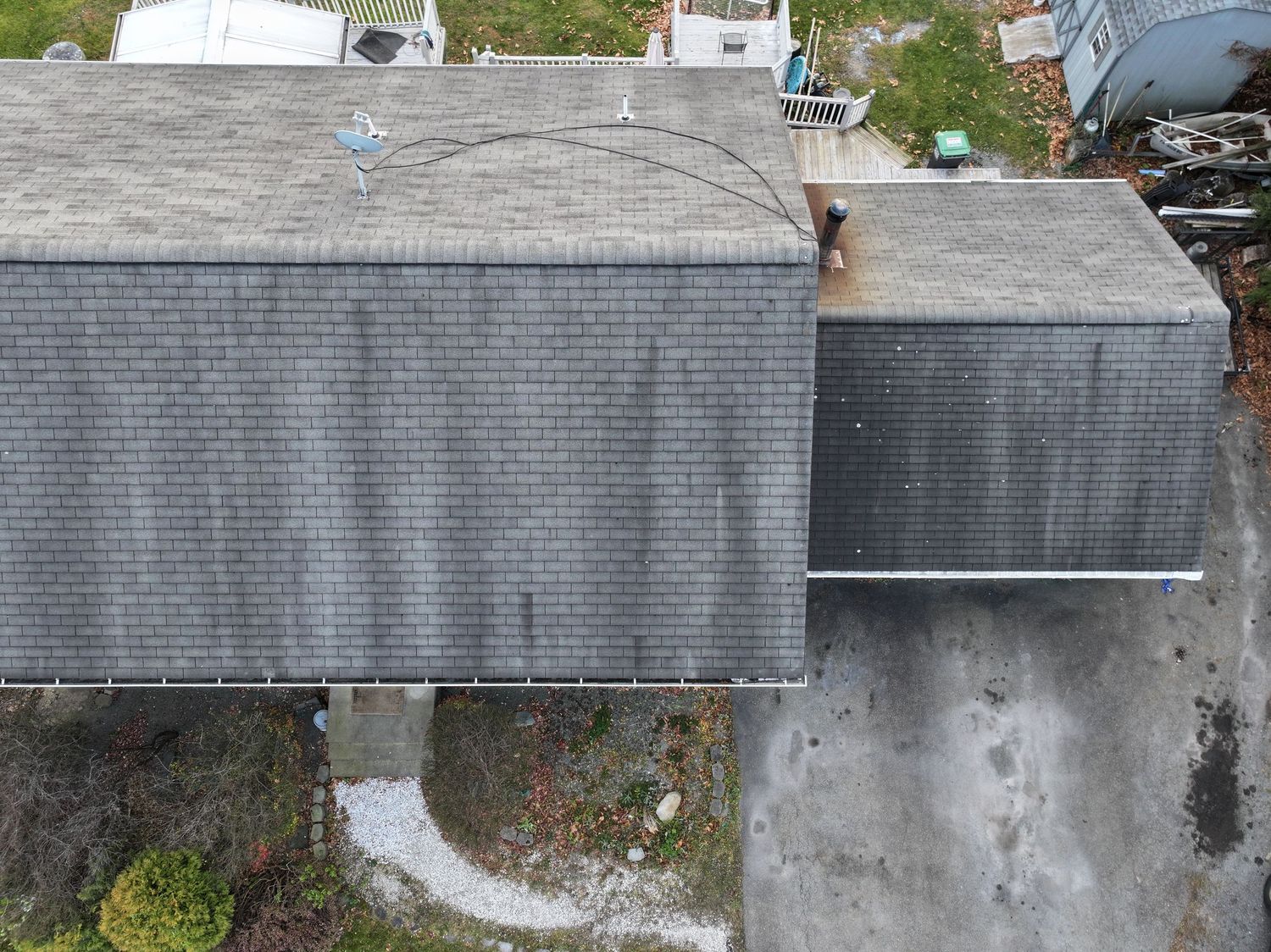 Aerial view of a residential rooftop with grey shingles and gutters against a green landscape background.