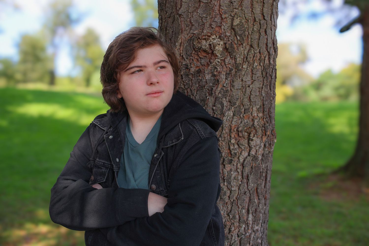 A series of four similar photos showing someone in a black jacket leaning against a tree trunk in a park setting.