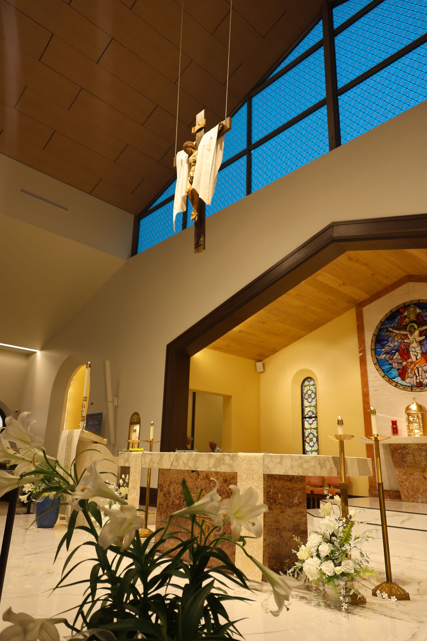 Interior view of a modern church sanctuary with blue skylights and white walls showcasing stained glass windows and plants.