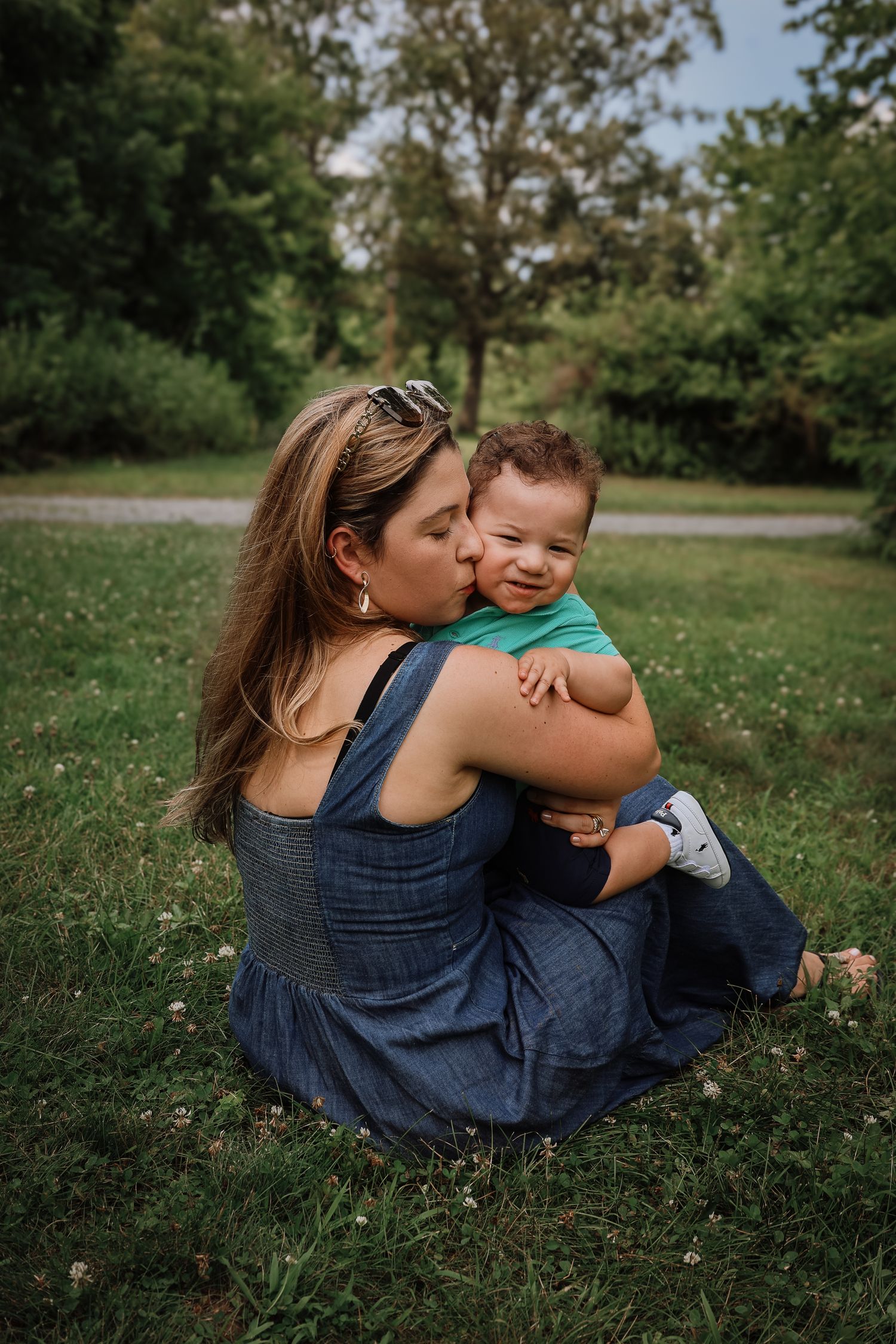 Parent and child share tender moments while sitting together in a grassy field on a sunny day.
