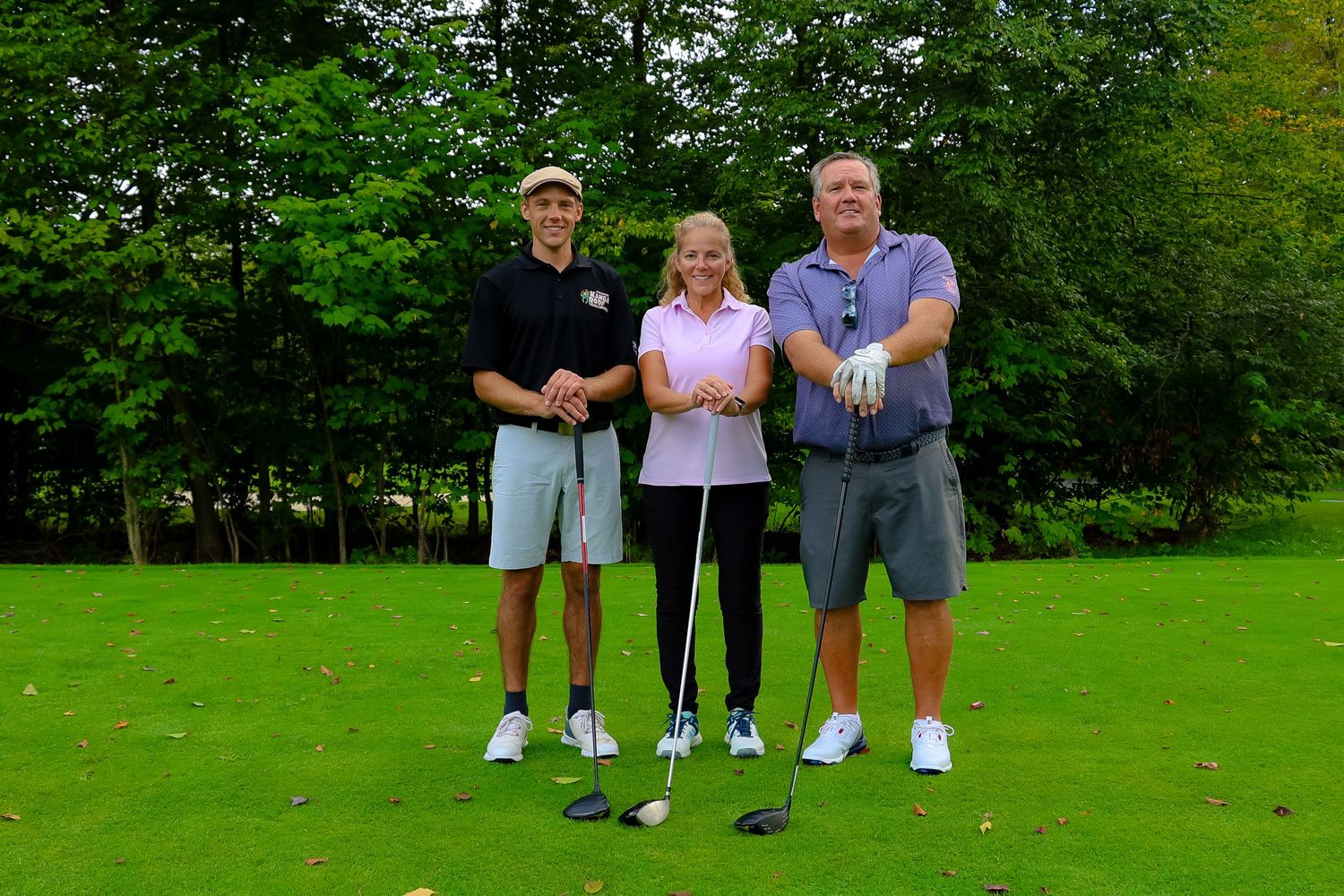 A group of golfers standing together on a lush green golf course with trees in the background.