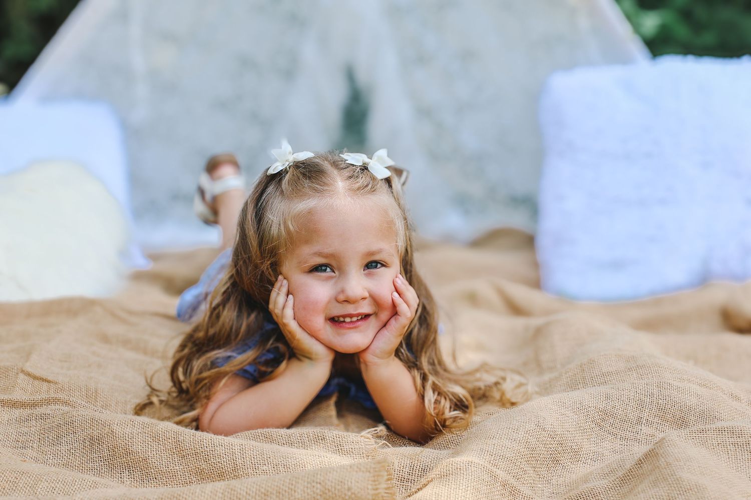 A person lies on a sandy beach blanket with a playful expression and flowing hair in the sunlight.