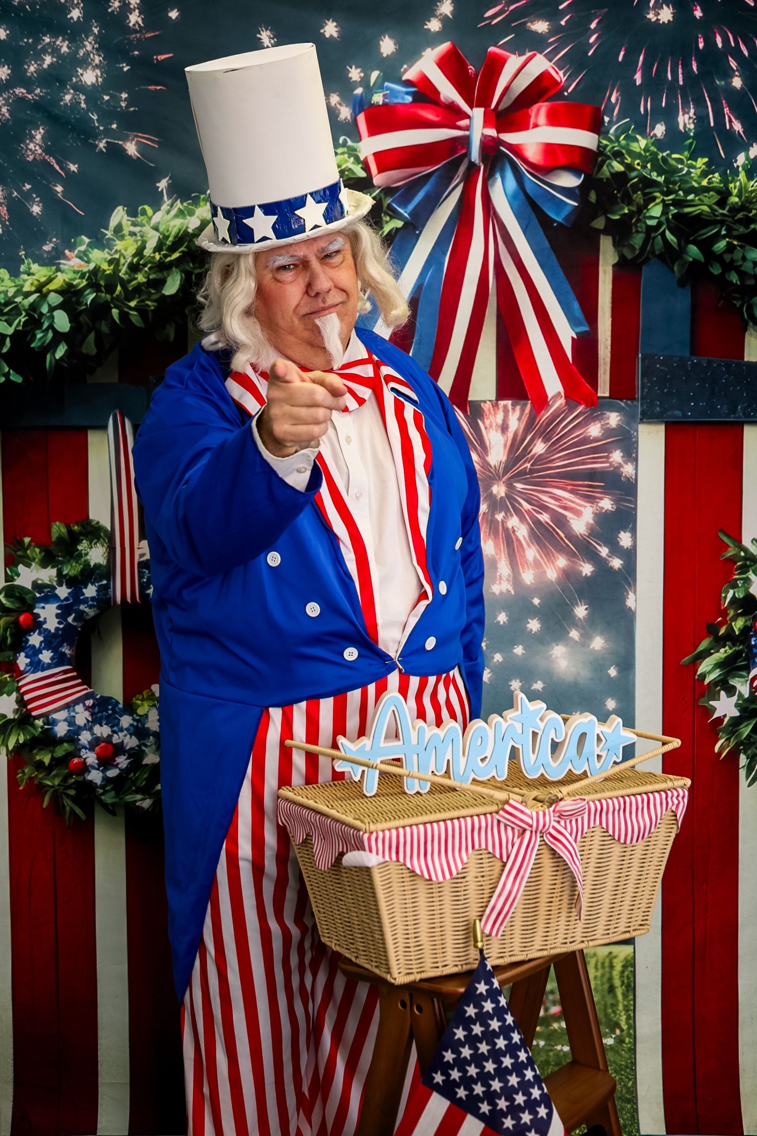 Uncle Sam costume character pointing forward with American flag decorations and fireworks backdrop.