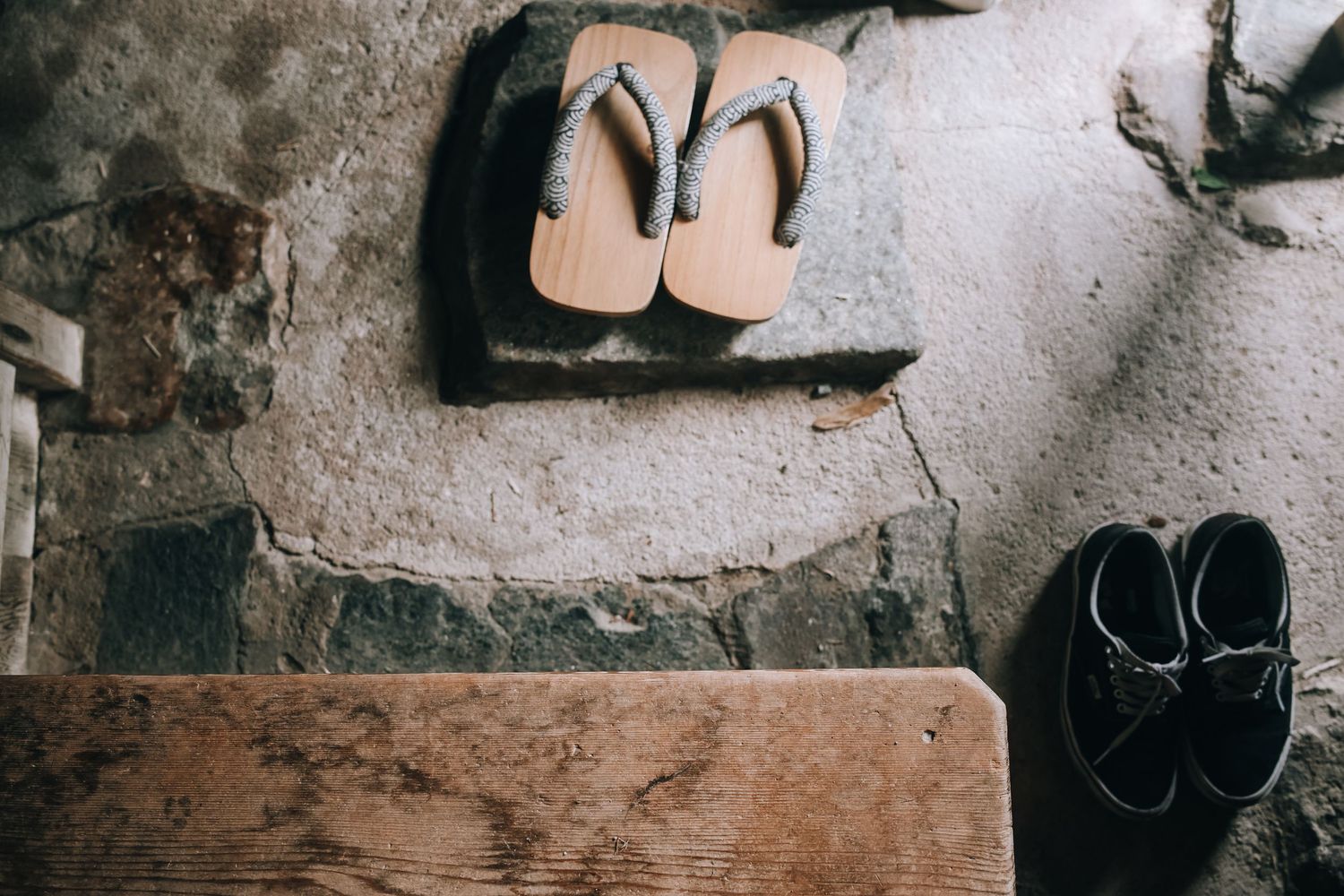Traditional Japanese wooden geta sandals and black leather shoes resting on rustic stone steps.