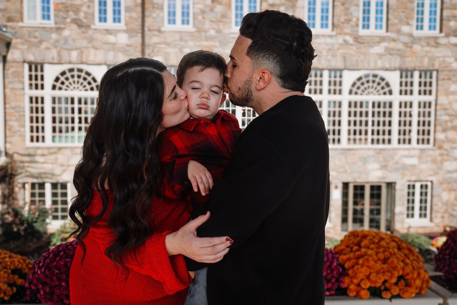 A couple shares romantic moments in front of a historic stone building with autumn decorations.