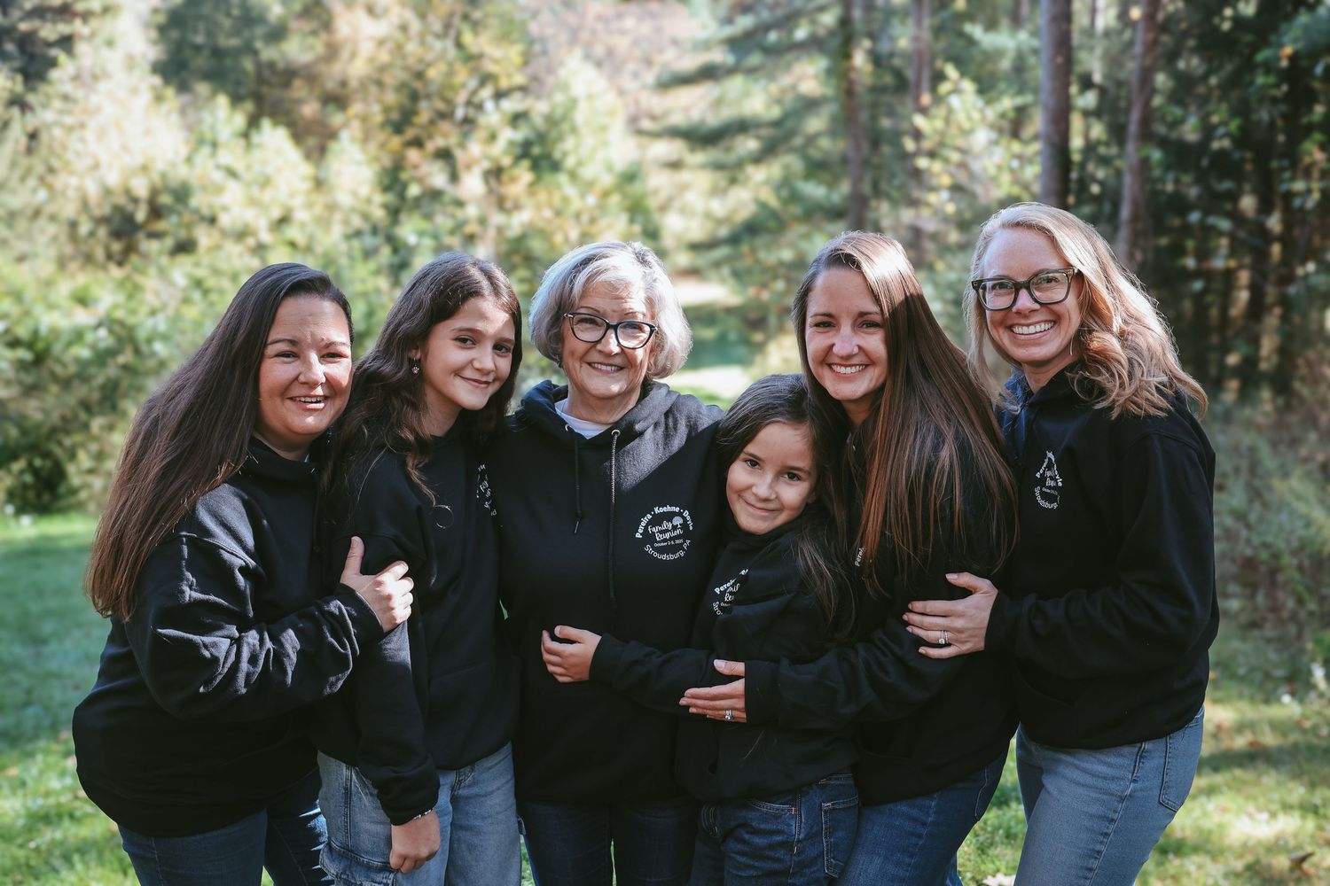 A group of people wearing matching black outfits pose together outdoors in a natural setting.