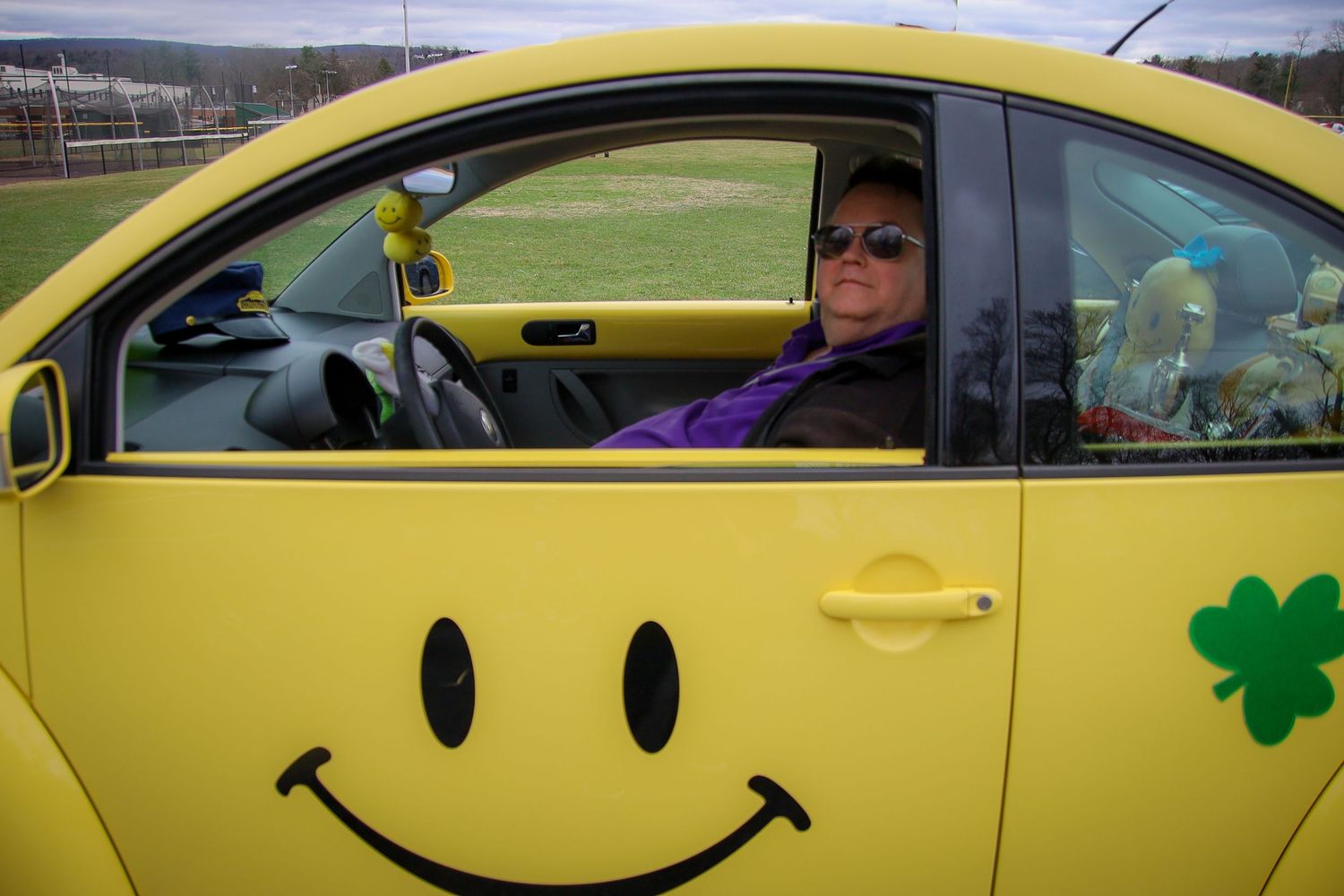A bright yellow car with a smiley face decal and shamrock decorations drives along the road.