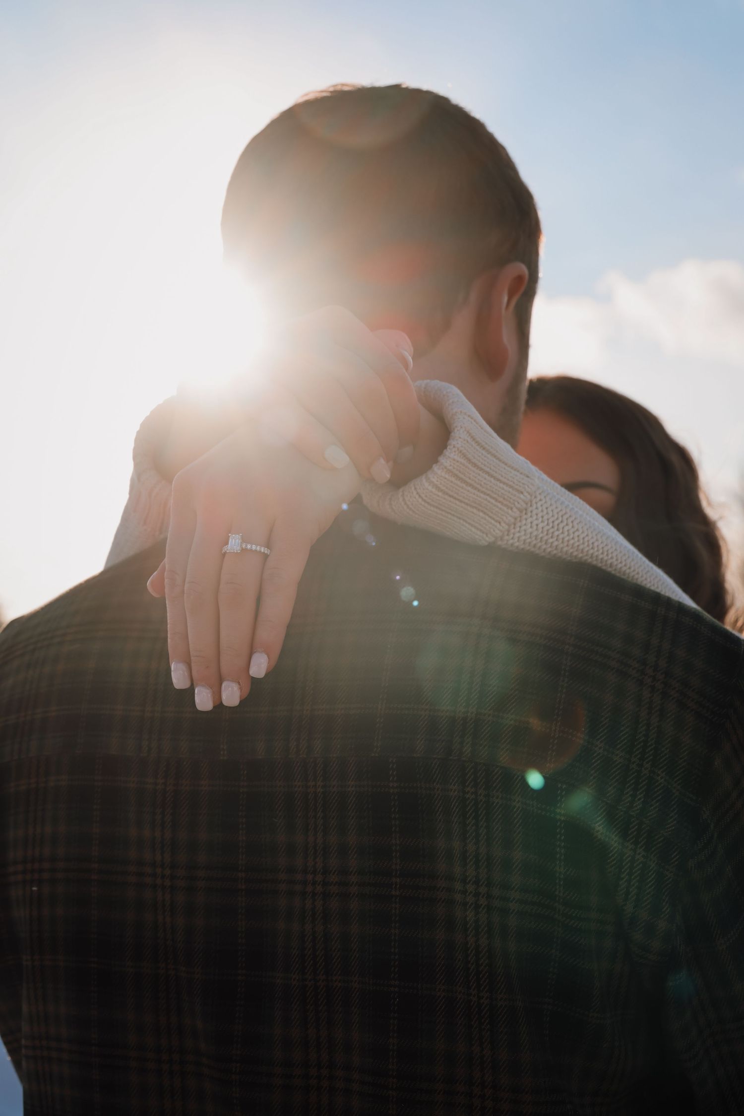 A romantic silhouette of a couple embracing in warm sunlight with lens flare creating a dreamy atmosphere.