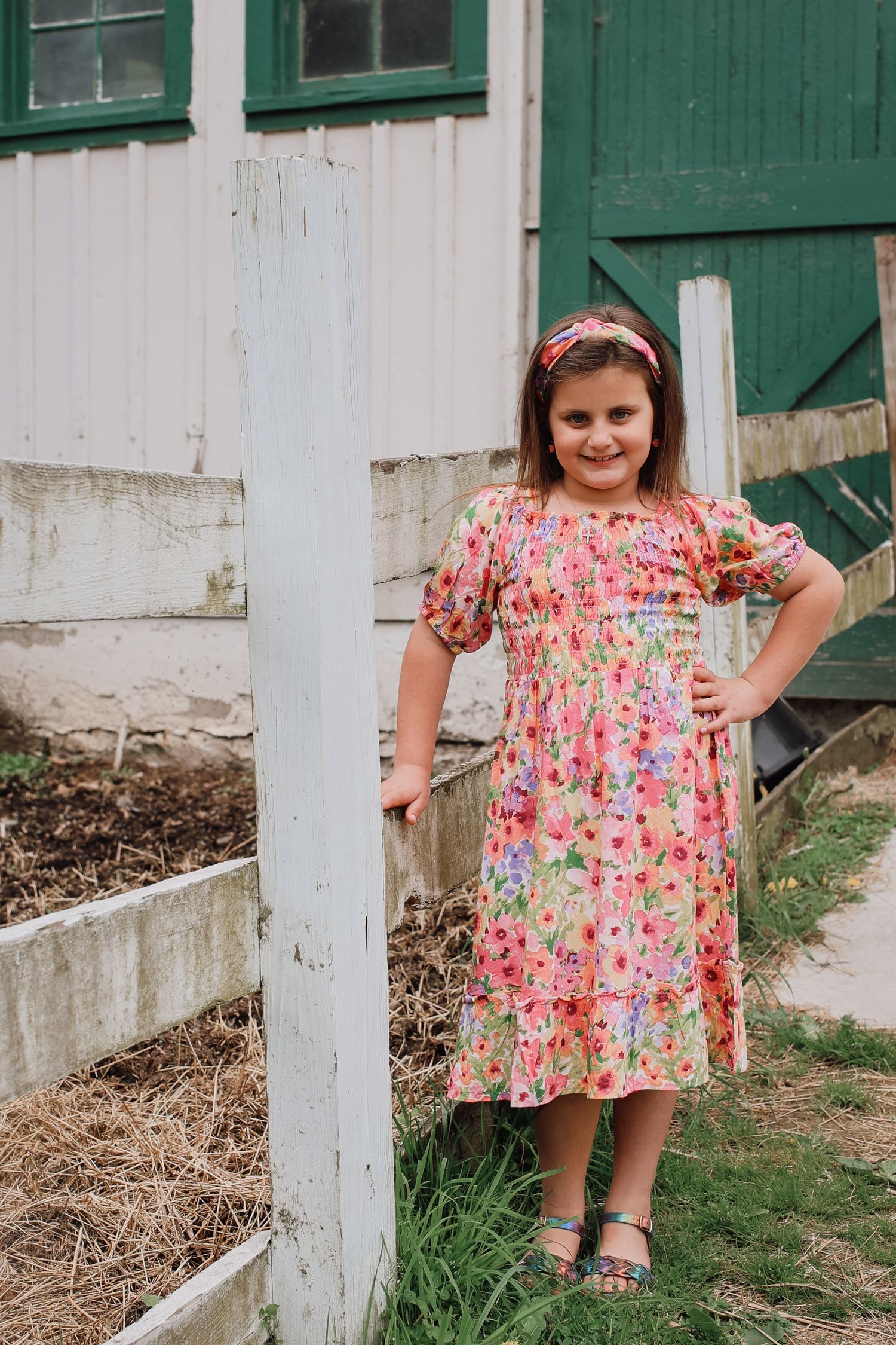 A floral print dress stands out against a rustic white and green barn backdrop in a countryside setting.