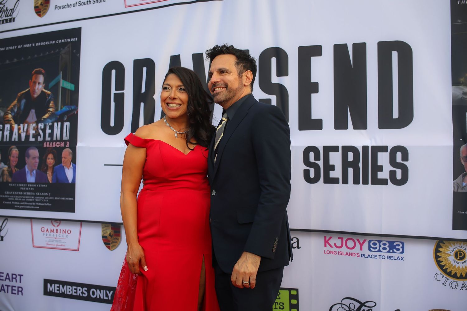 A couple poses together at a red carpet event in front of a Grandsend Series backdrop.