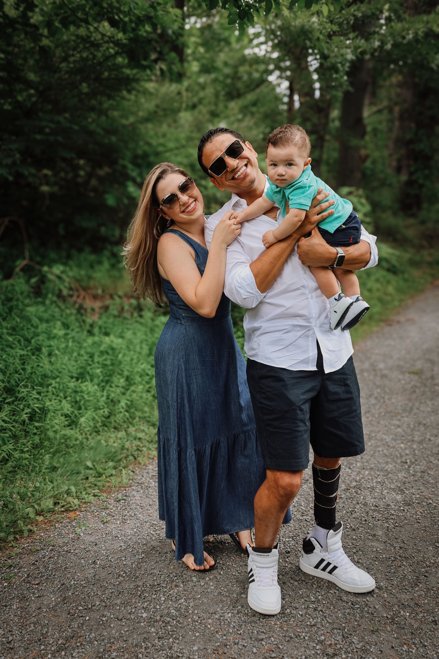 A family shares playful moments together on a tree-lined path in casual summer outfits.