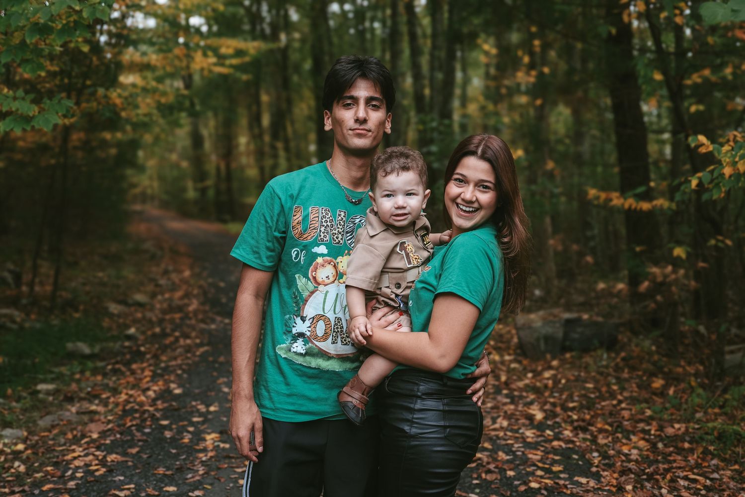 A family enjoys an autumn photoshoot in a forest filled with fallen leaves and golden light.